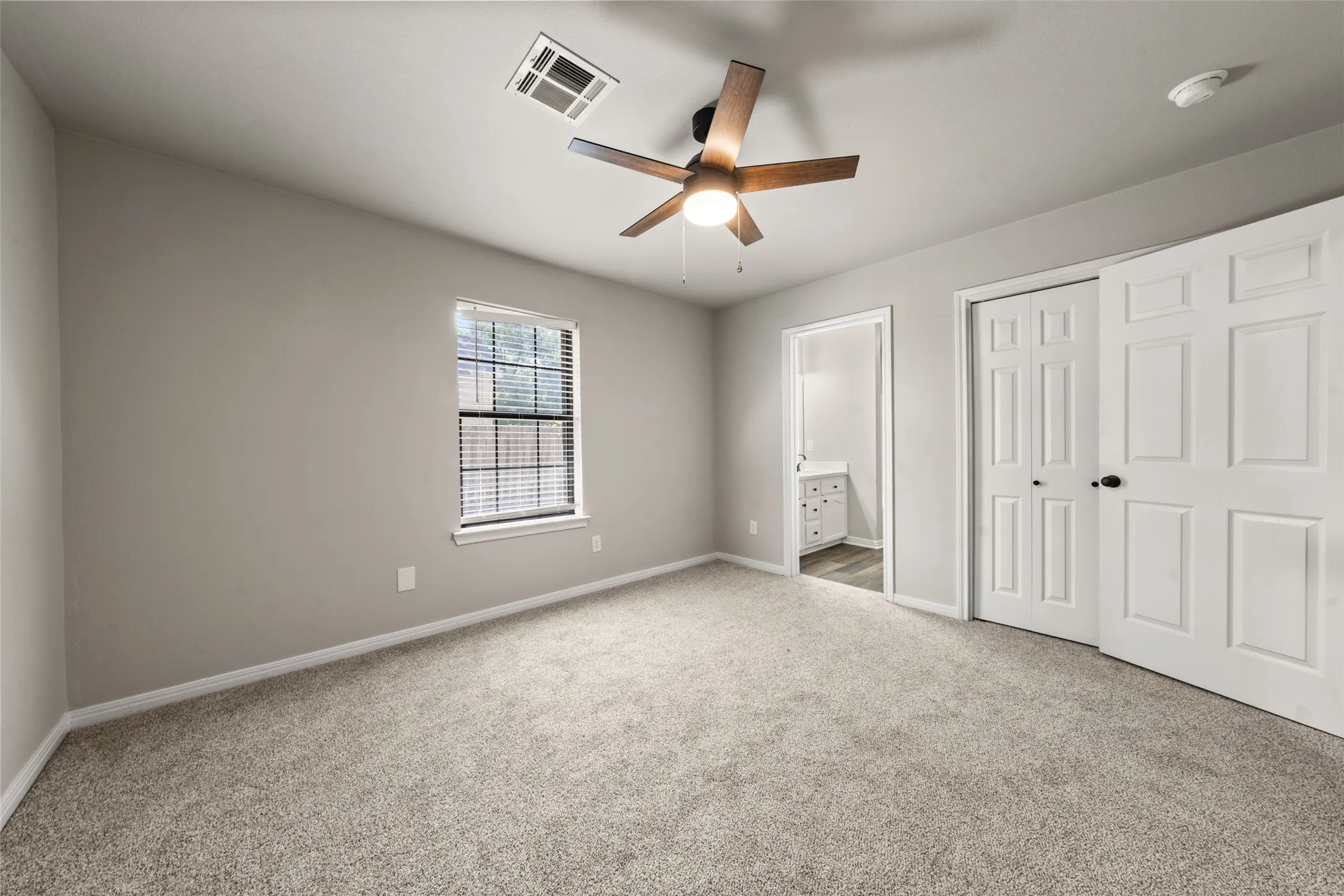 Neutral-toned walls, wood-finish ceiling fan, window with blinds, carpeted flooring, and a six-panel bi-fold closet door