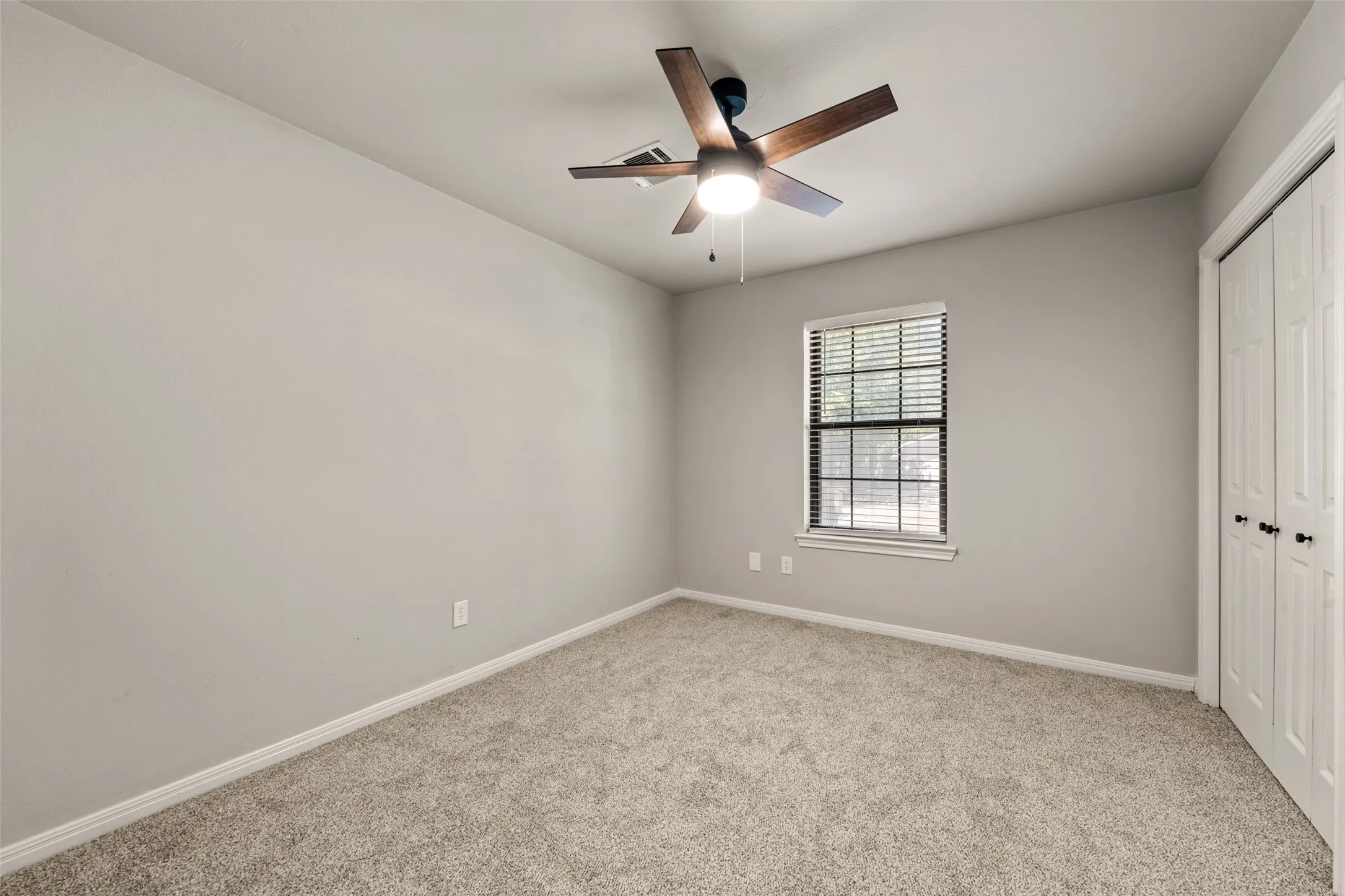 Neutral-toned walls, wood-finish ceiling fan, window with blinds, and light-colored carpet flooring