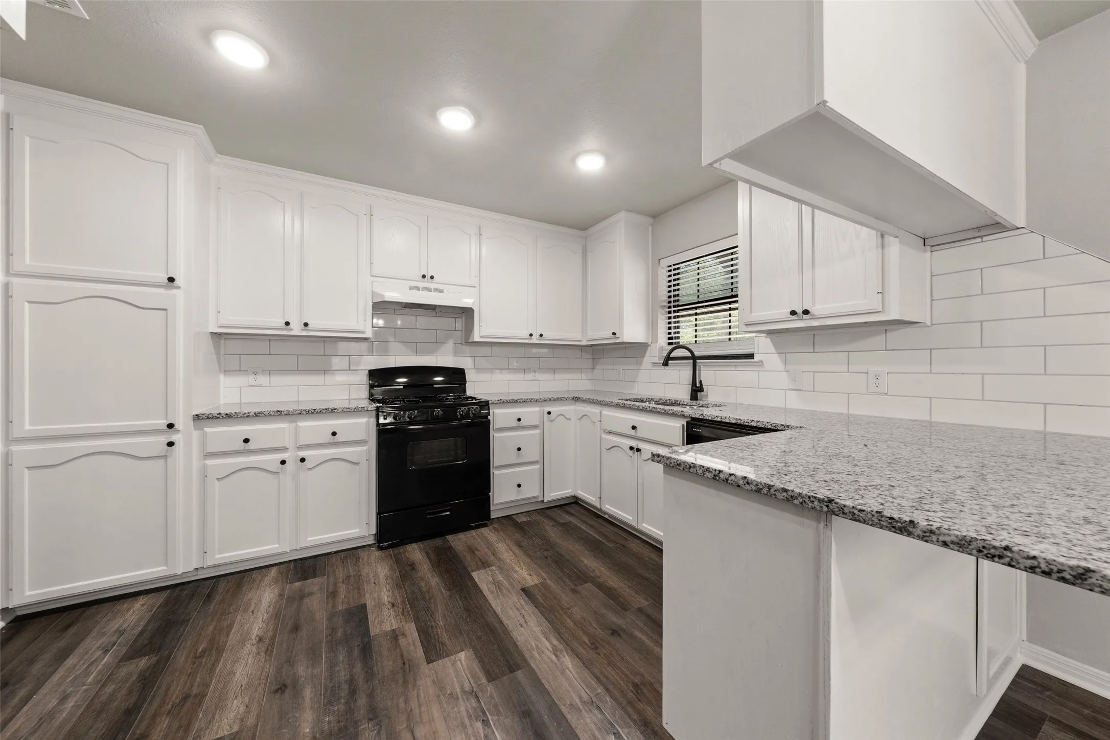 Kitchen featuring white cabinetry, dark wood-finish flooring, a tile backsplash, light-colored countertops, and a black range
