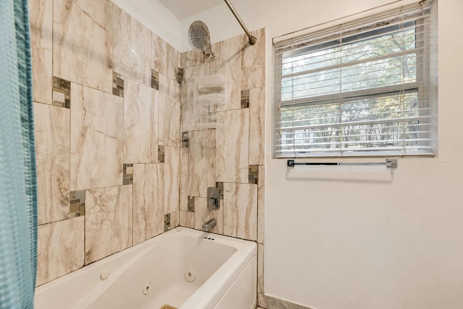 Tiled shower surround with decorative mosaic accents, integrated shower head, and tub filler