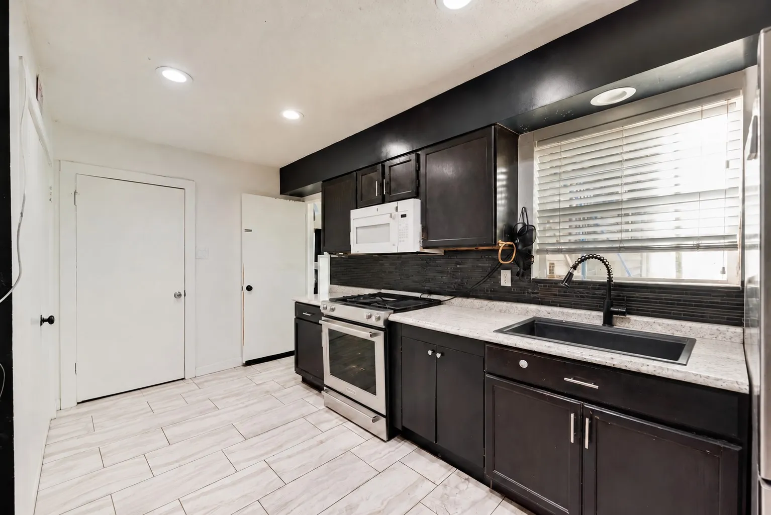 Recessed ceiling lighting, wood-finish tile flooring, dark wood-finish cabinetry, stainless steel range, and a black sink with a matte black faucet
