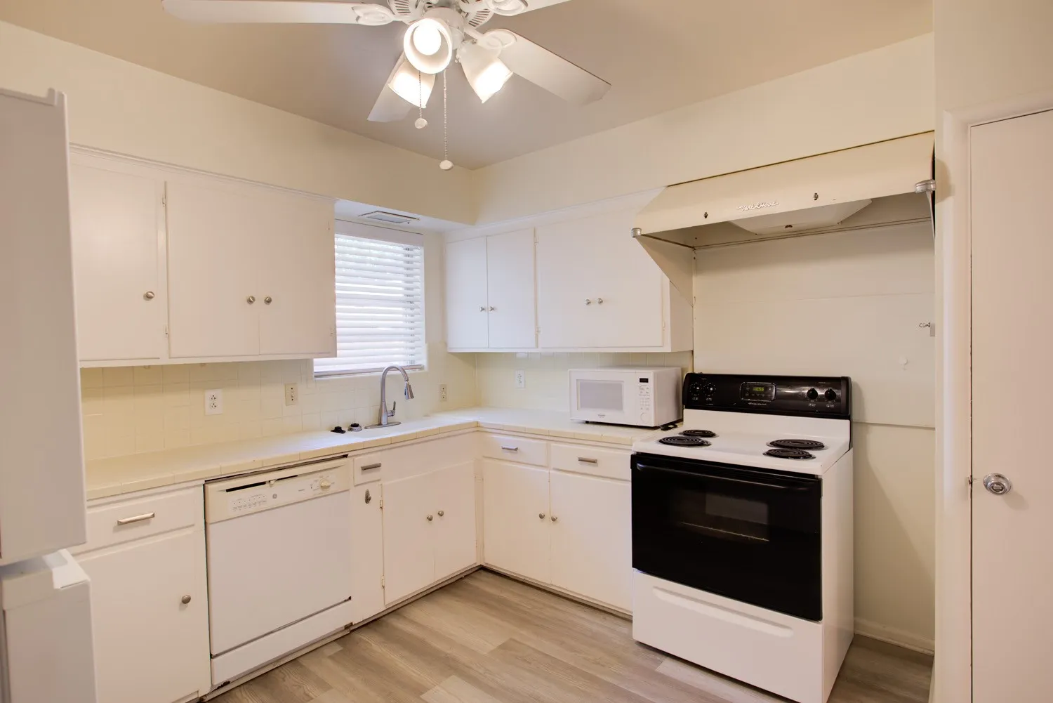 Kitchen featuring white cabinetry, tile countertops, dishwasher, and wood-finish vinyl flooring