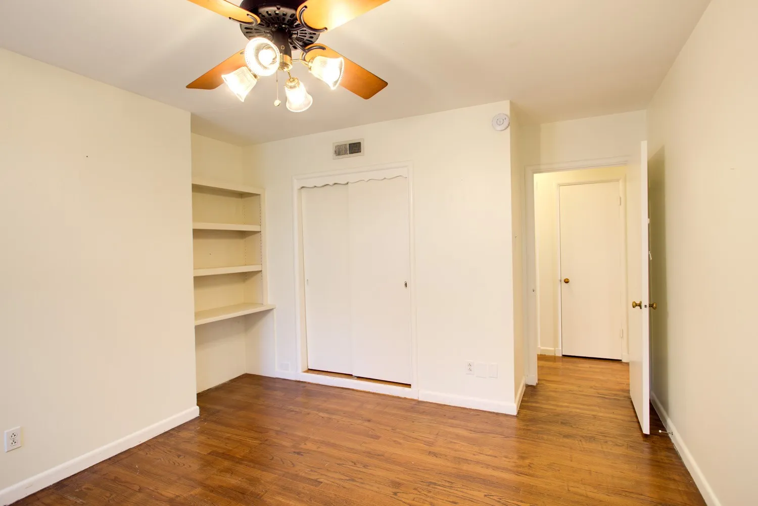 Bedroom with hardwood floors, built-in shelving, and bi-fold closet doors