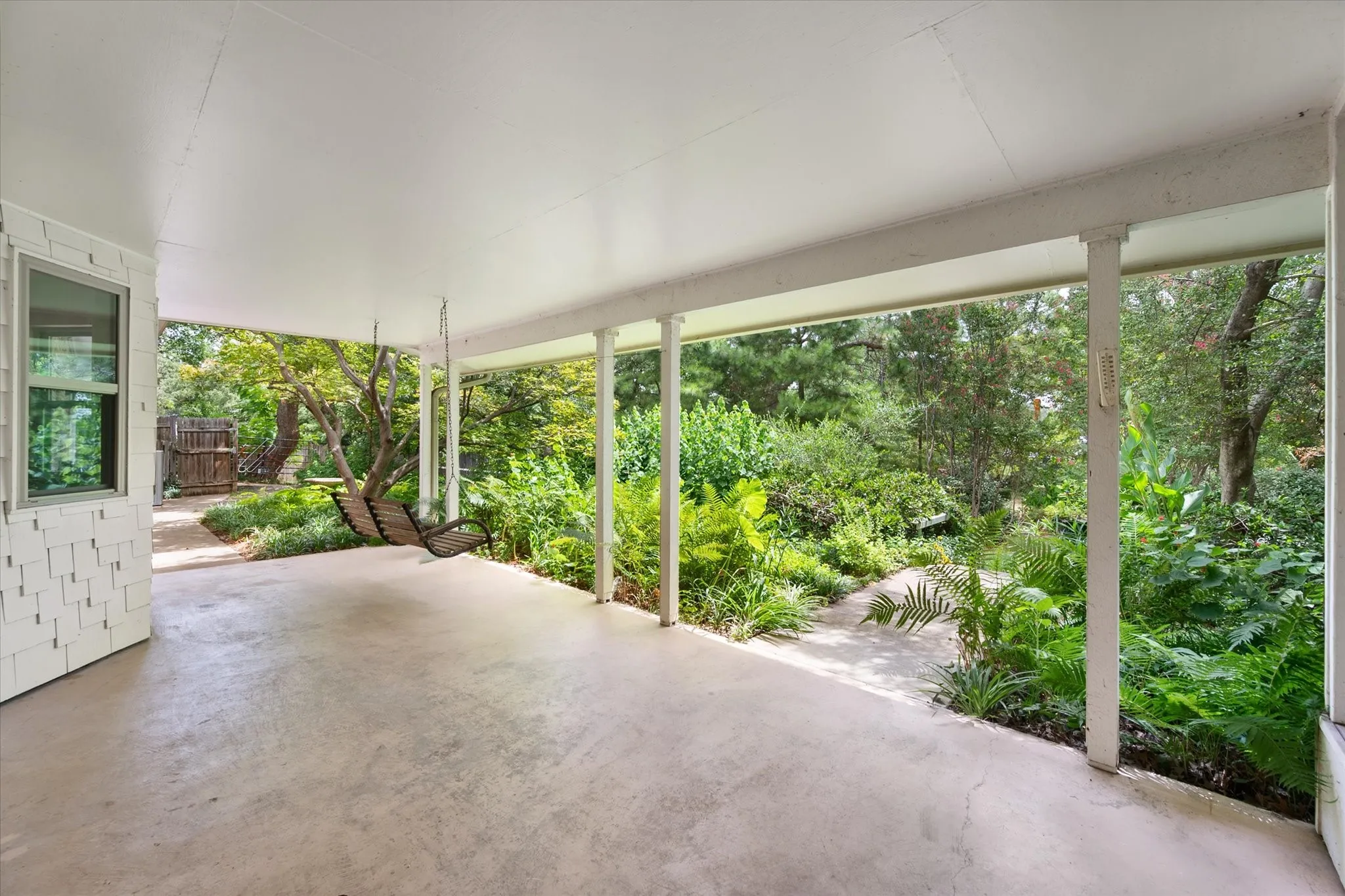 Large covered outdoor patio with a concrete surface and a lush natural landscape