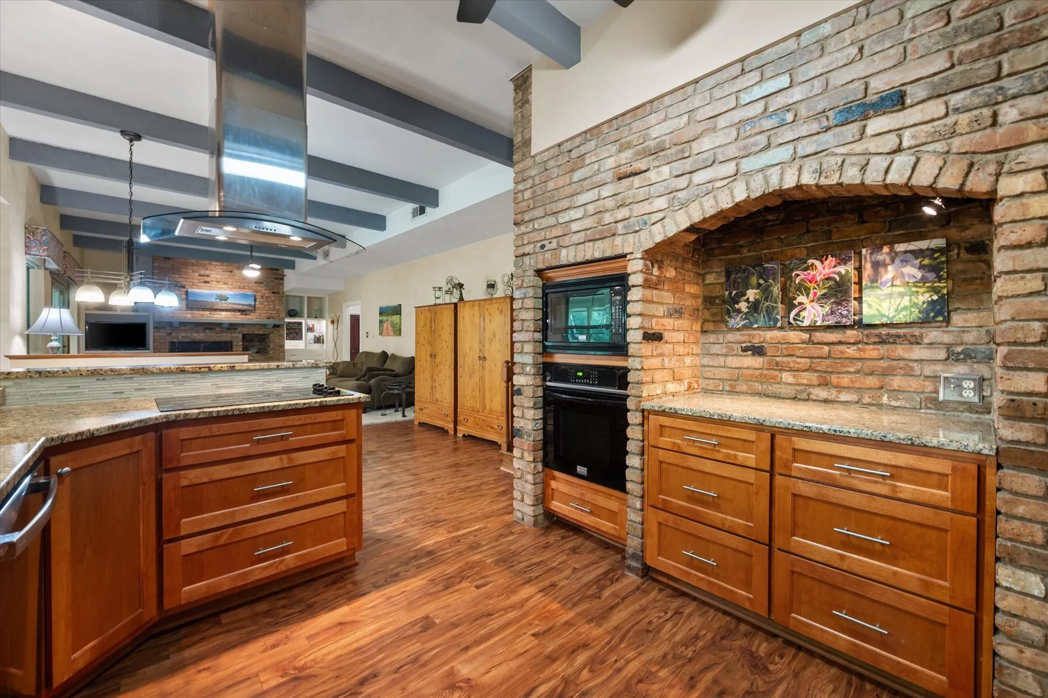 Built-in brick oven archway, rich wood-finish flooring, updated natural wood cabinetry, light granite countertops, and a stainless steel range hood.
