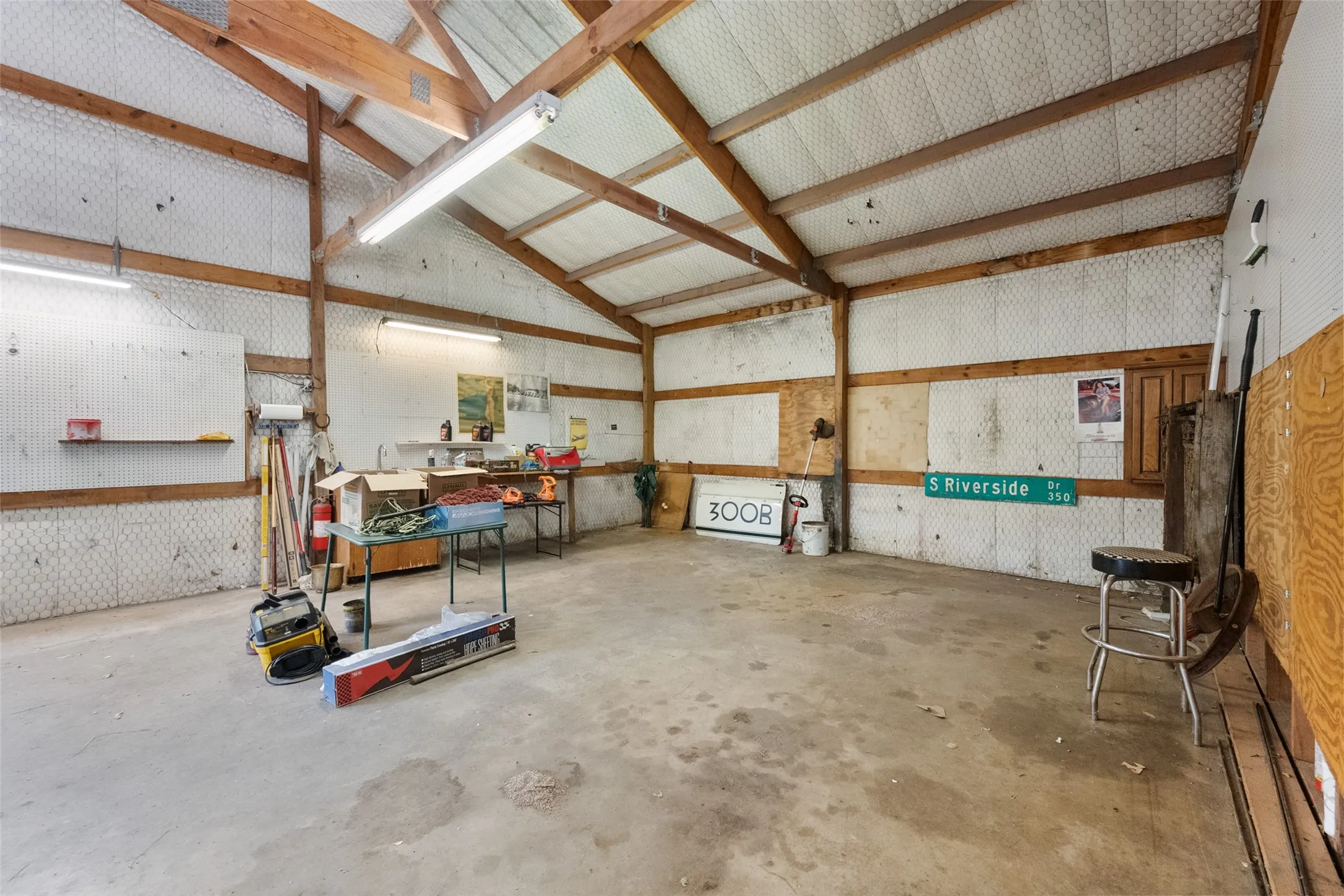 Another view of the spacious industrial interior featuring exposed wood beams, corrugated metal wall panels, concrete flooring, and fluorescent overhead lighting.
