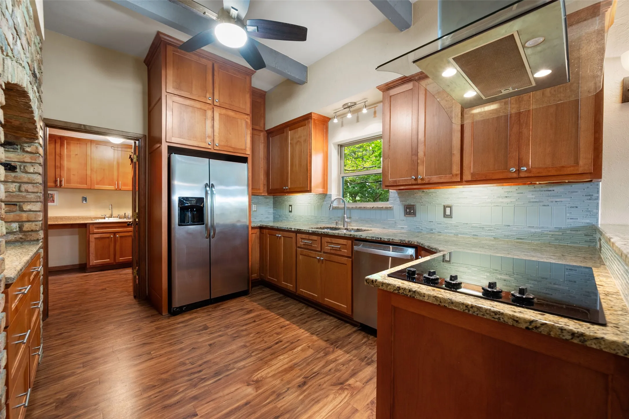 Kitchen featuring wood-finish flooring, updated wood cabinetry, granite countertops, and a pretty tile backsplash