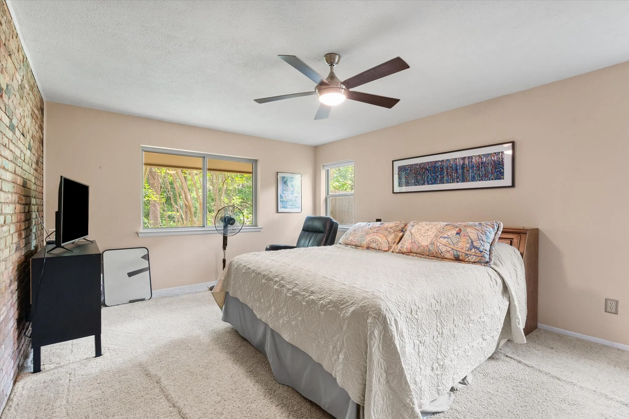 Primary Bedroom is located downstairs and features exposed brick accent wall, light-colored carpeting, views of the backyard and a ceiling fan with integrated lighting