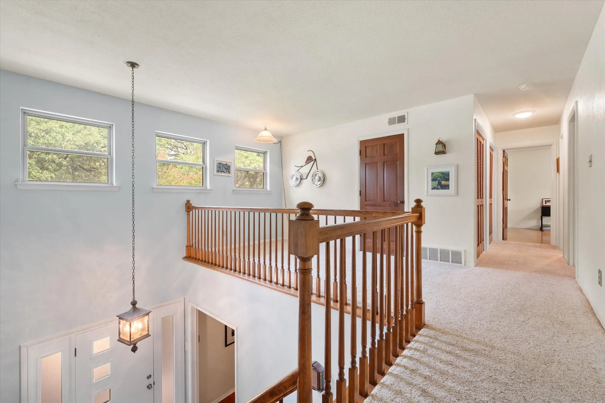 Upper-level landing featuring wood balusters, light-colored carpet flooring and an access door to a walk-out attic area.