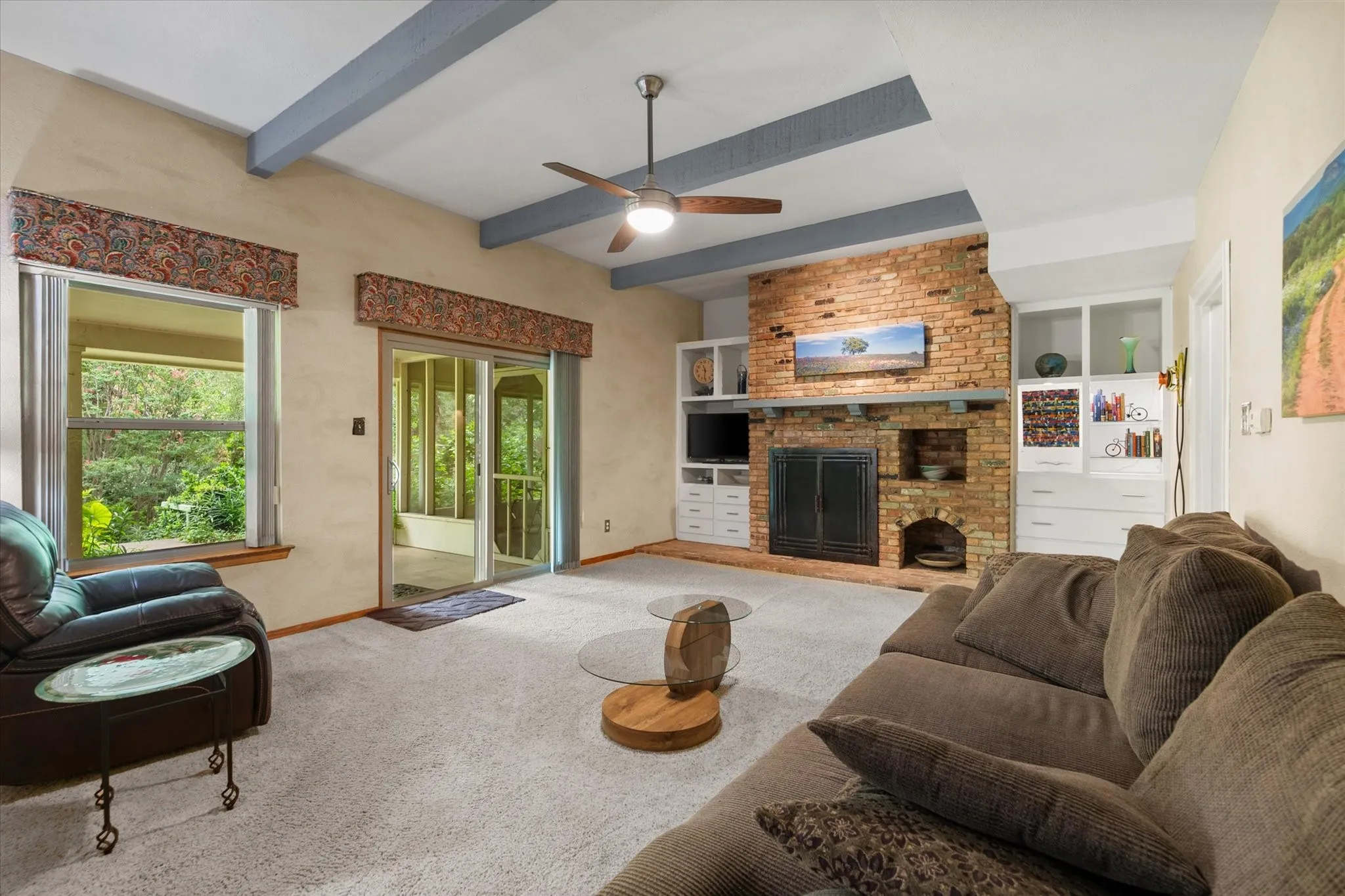 Exposed ceiling beams, brick fireplace with hearth, built-in cabinetry, ceiling fan, and sliding glass door leading to the backyard covered patio and screened porch area.