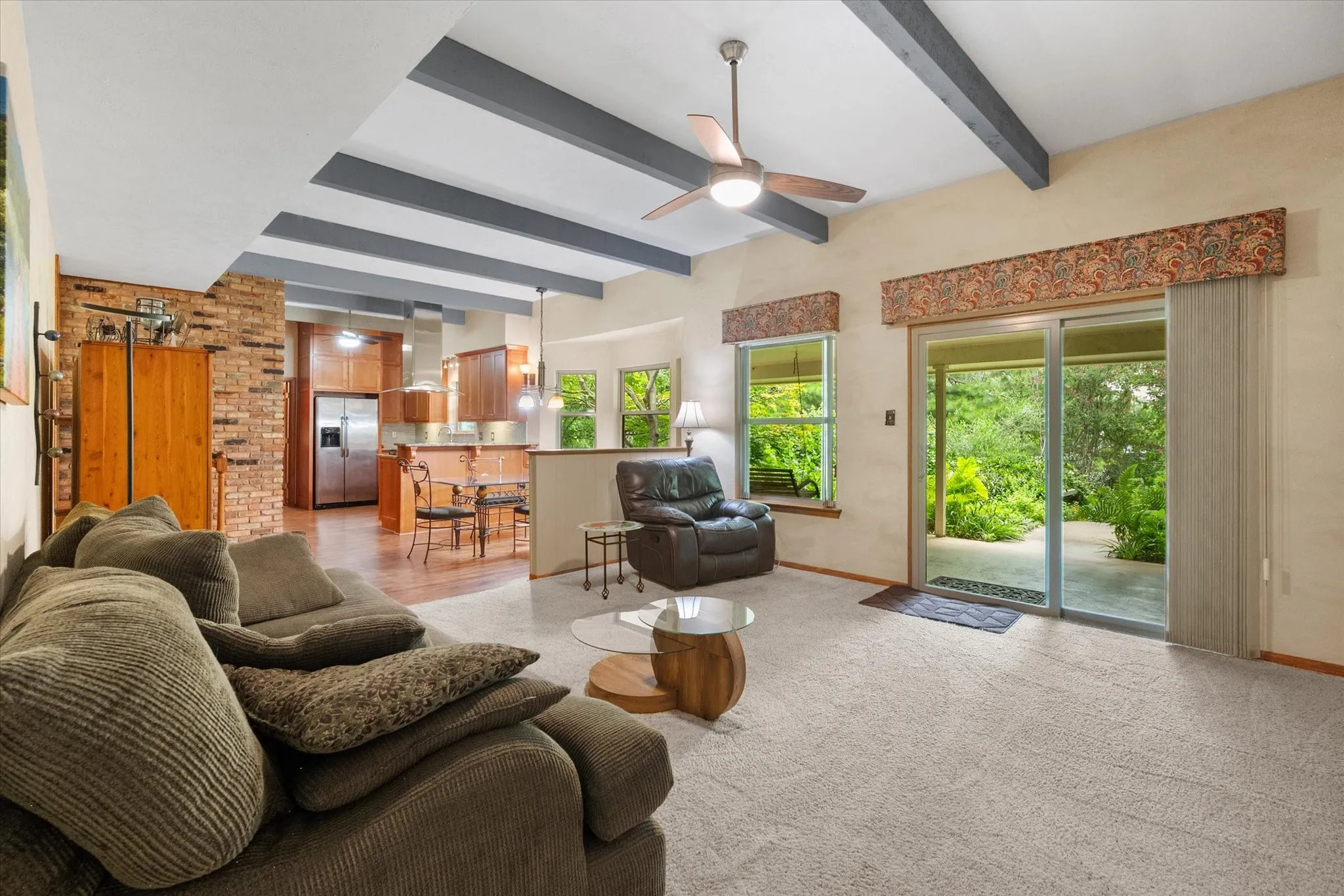 Open concept Den features a vaulted ceiling with exposed beams, ceiling fan, carpet flooring, and sliding glass door with outdoor access to the backyard covered patio.