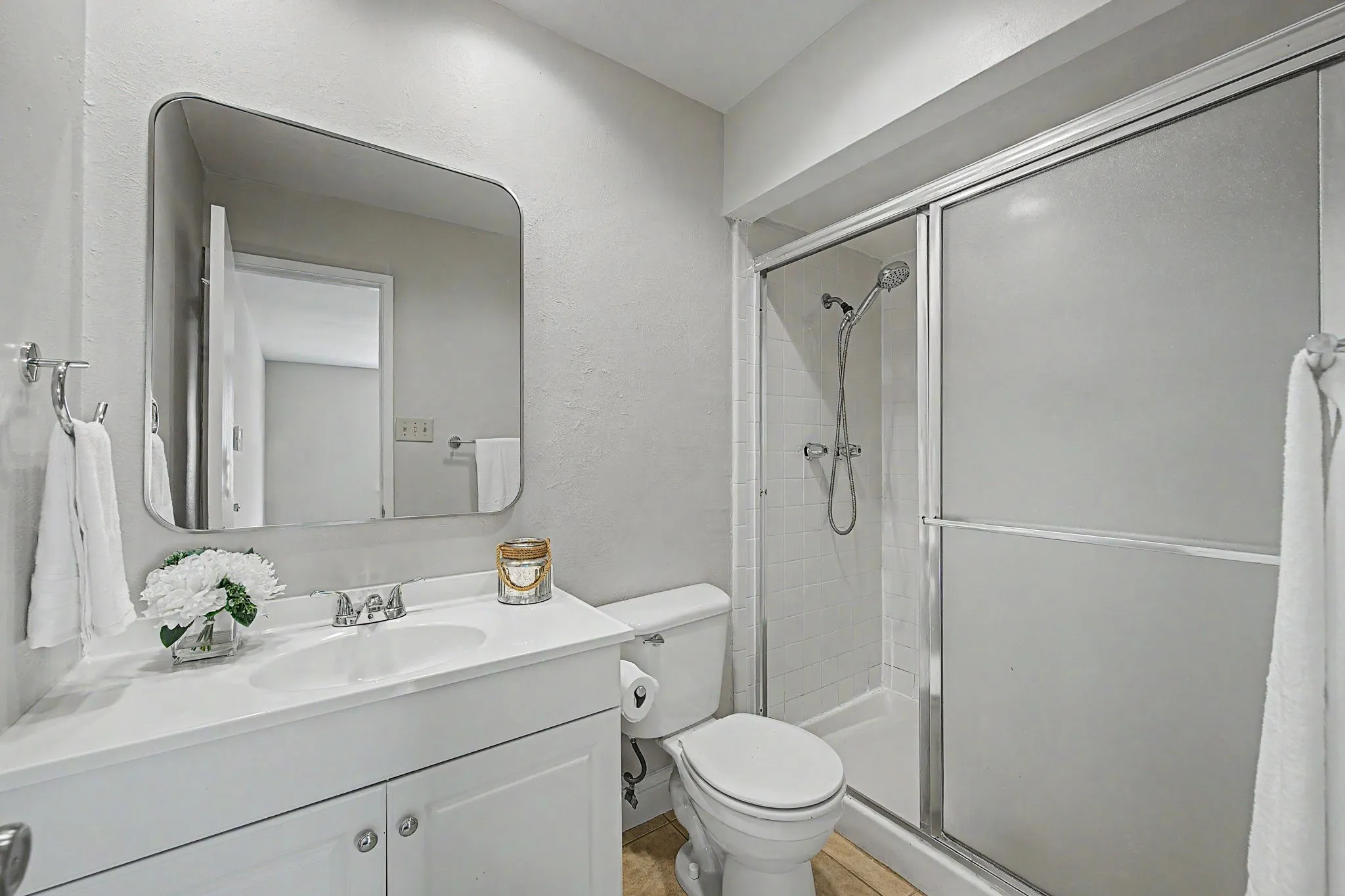 Stand up shower with sprayer, large framed mirror, toilet and vanity.