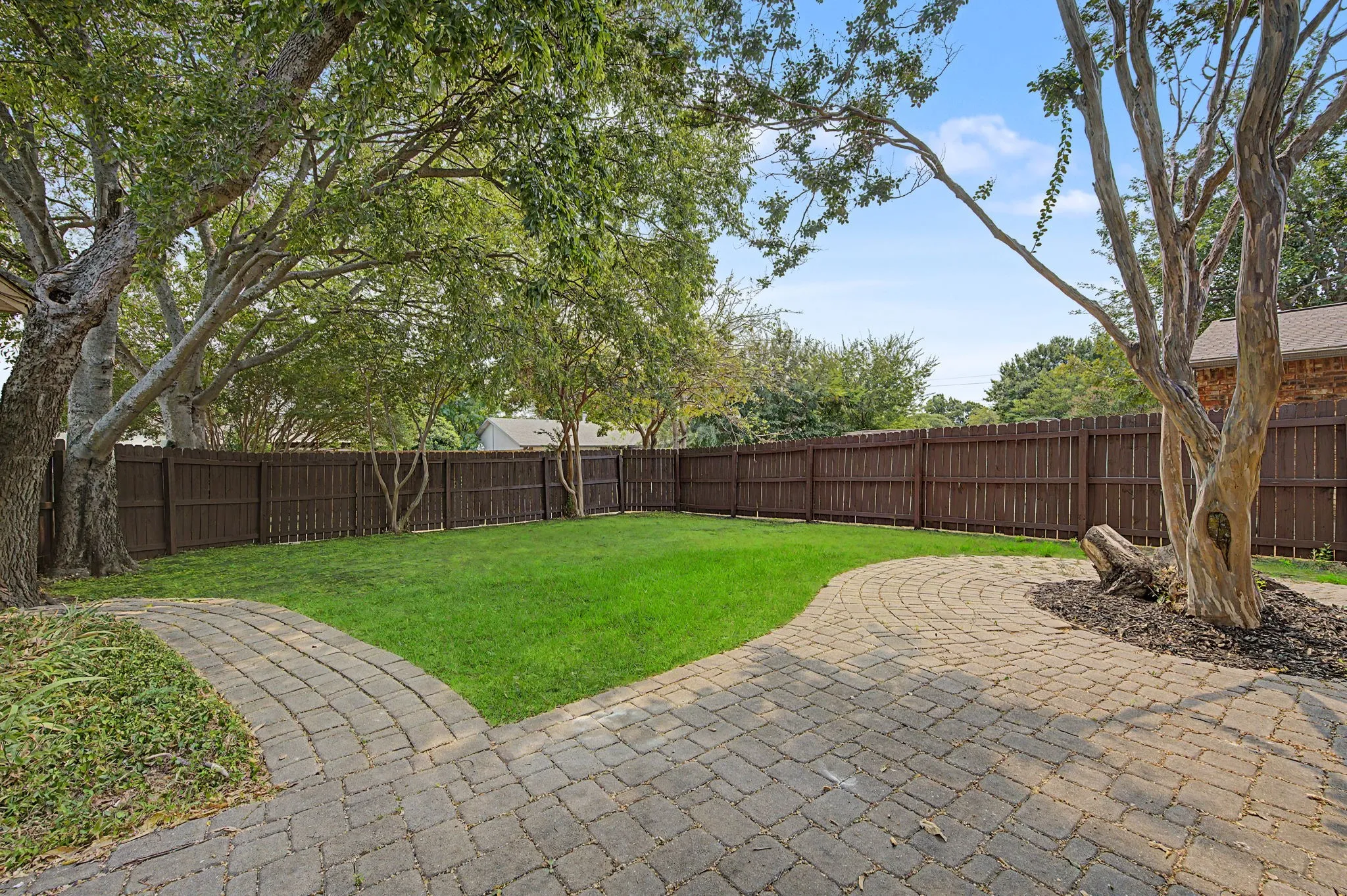Generous size back yard with mature trees, stained fence, and lovely cobblestone patio and pathway to the drivway.