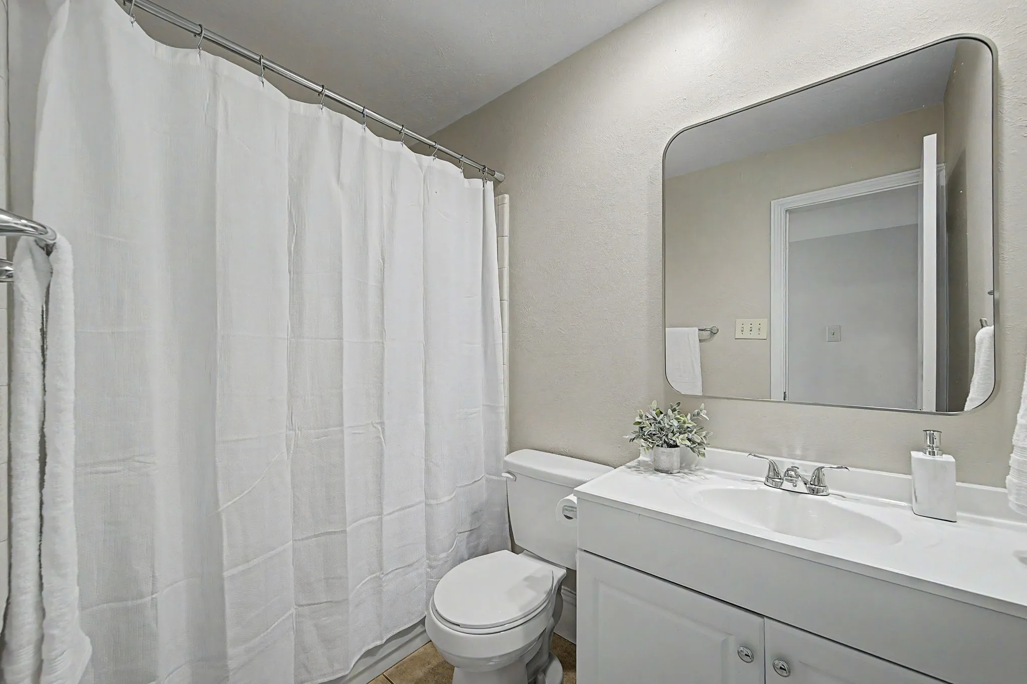 Secondary guest bathroom with tub/shower combo, framed mirror, toilet and vanity.