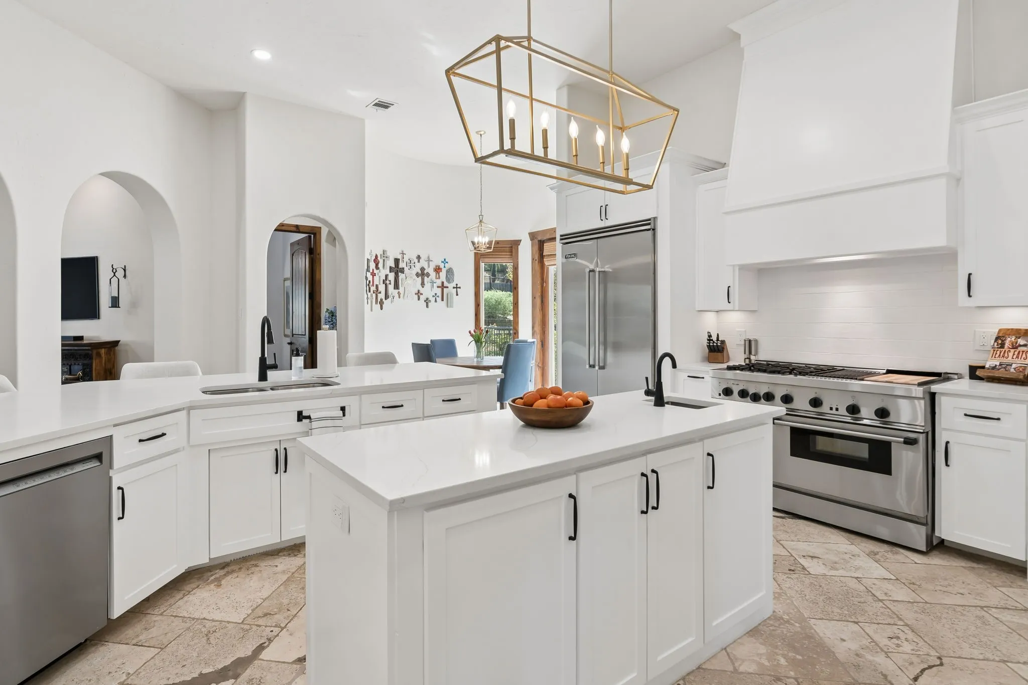 Gourmet kitchen featuring a large central island, white cabinetry, integrated stainless-steel appliances, a tile backsplash, and arched doorways