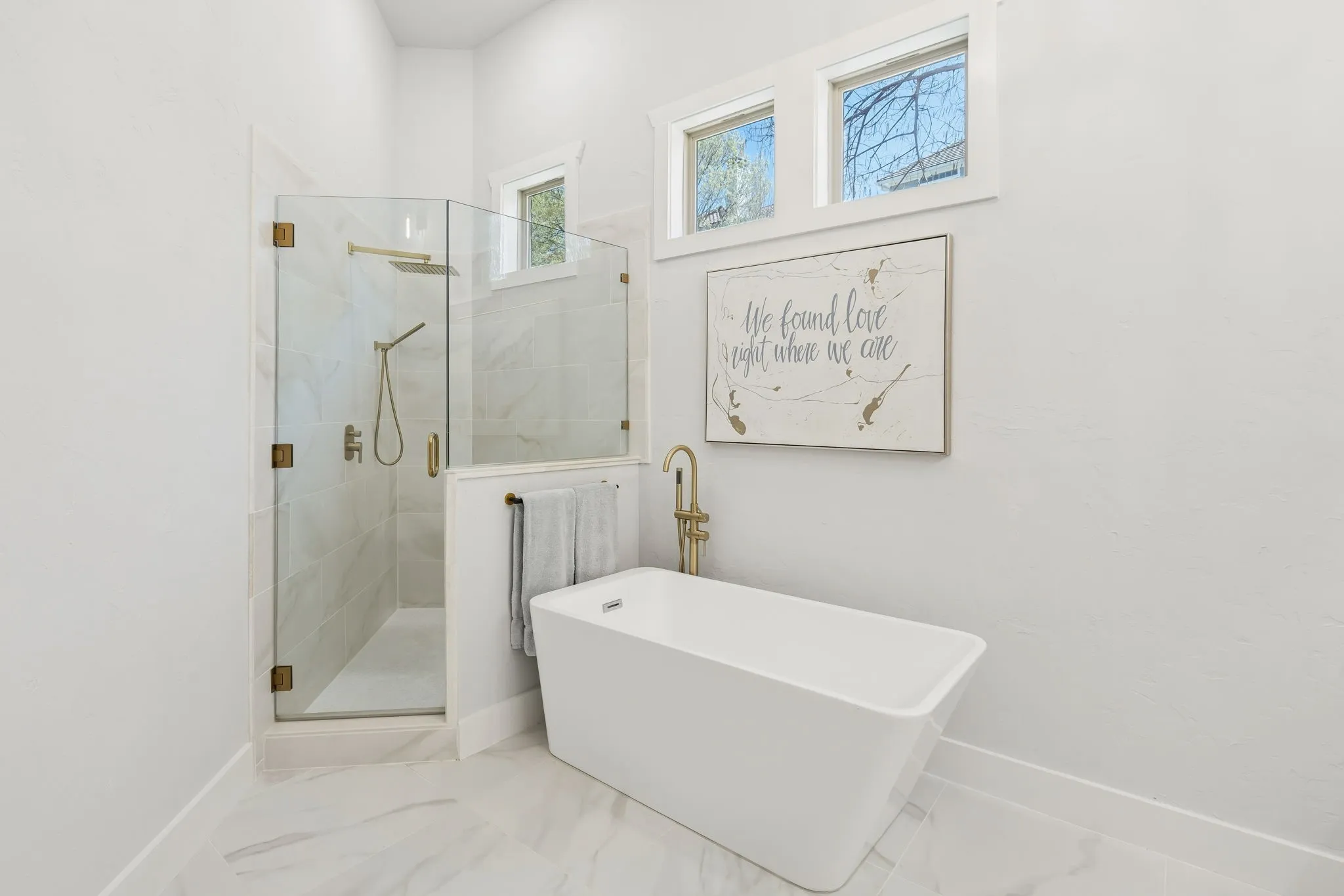 Freestanding soaking tub with gold-finish fixtures, a glass-enclosed shower, and light-toned tile flooring