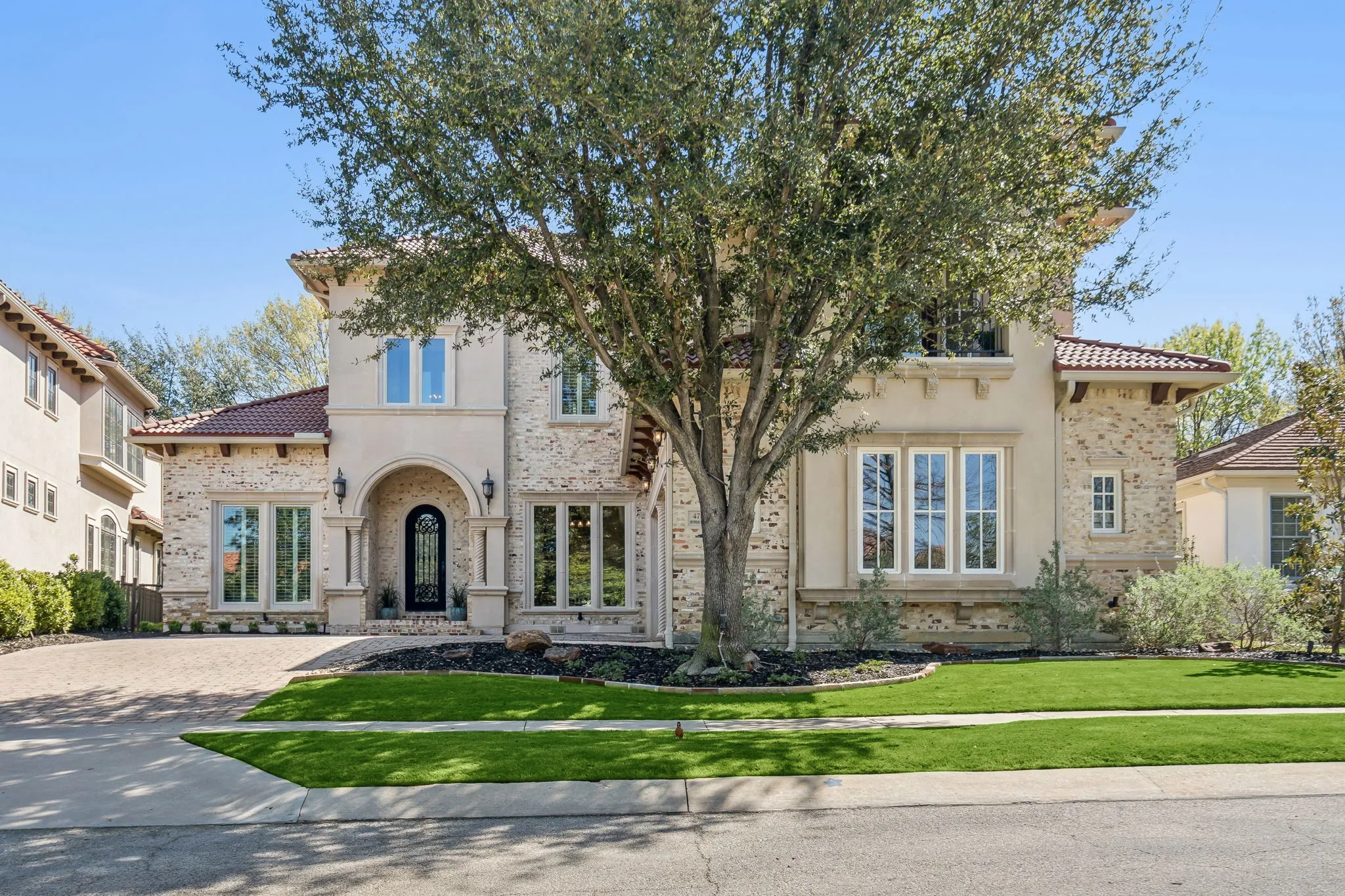 Mediterranean-style architecture with a stucco and stone exterior, arched entry, tiled roof, multiple window styles, and a paved driveway