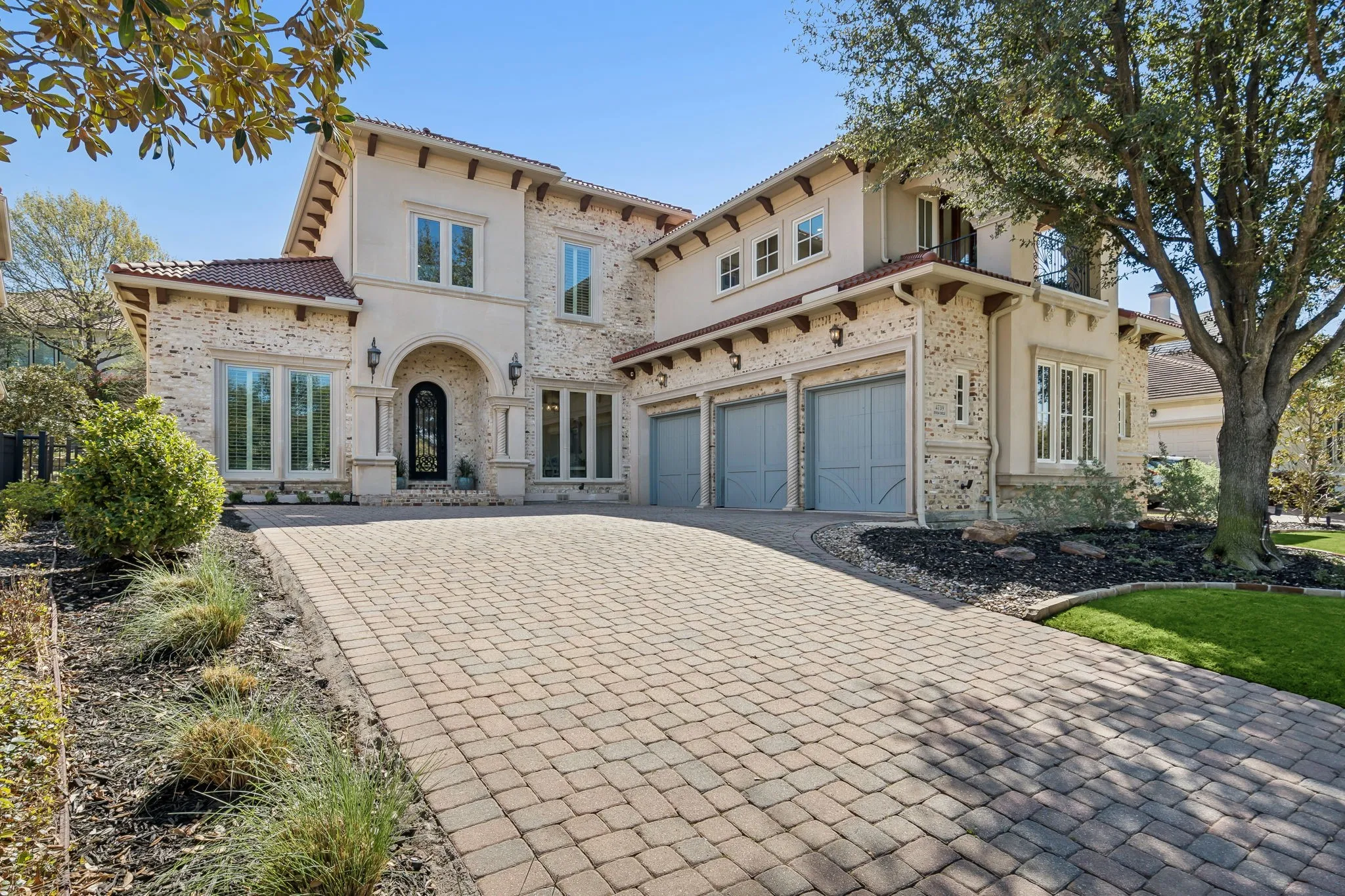 Stucco and stone exterior with a clay tile roof, arched entryway, and a three-car garage