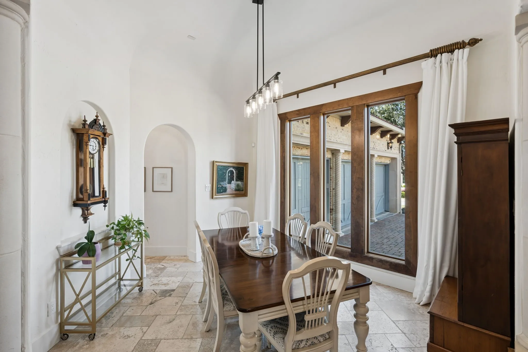Vaulted ceiling, arched doorways, tiled flooring, wood-framed windows, and a multi-bulb linear light fixture