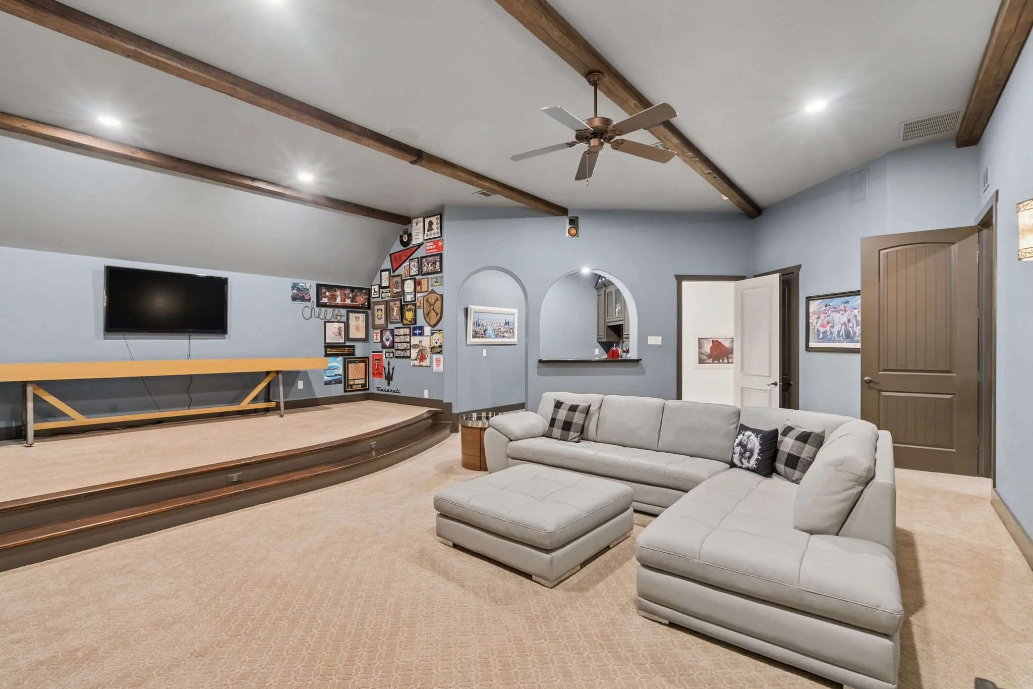 Vaulted ceiling with wood-finish beams, recessed lighting, ceiling fan, and a raised platform area