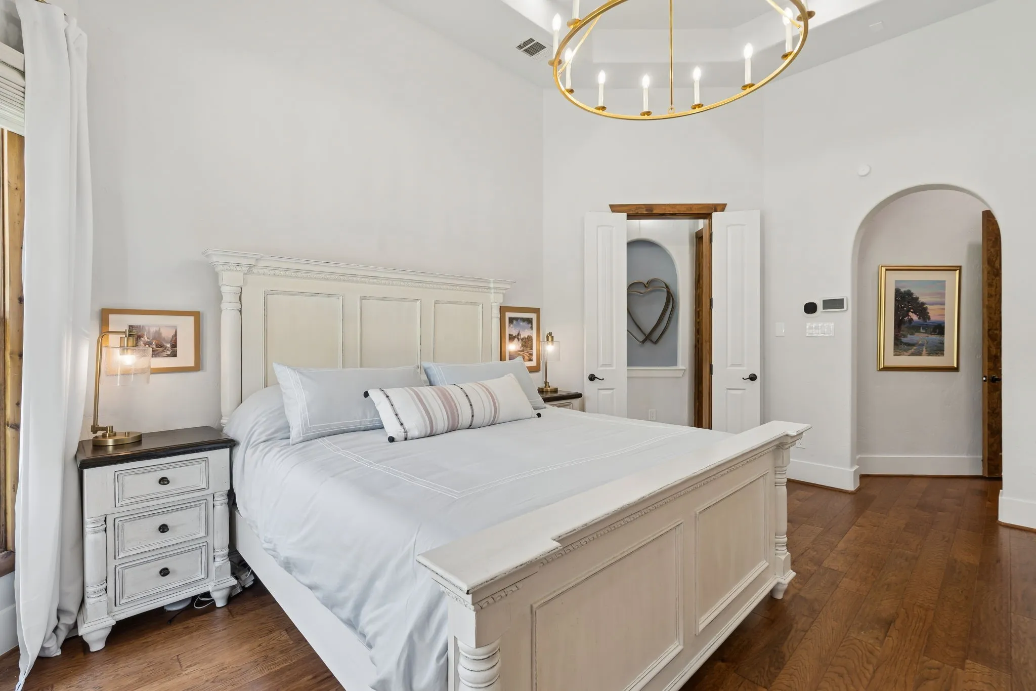 Tray ceiling with an elegant brass chandelier, archways, and wood-finish flooring