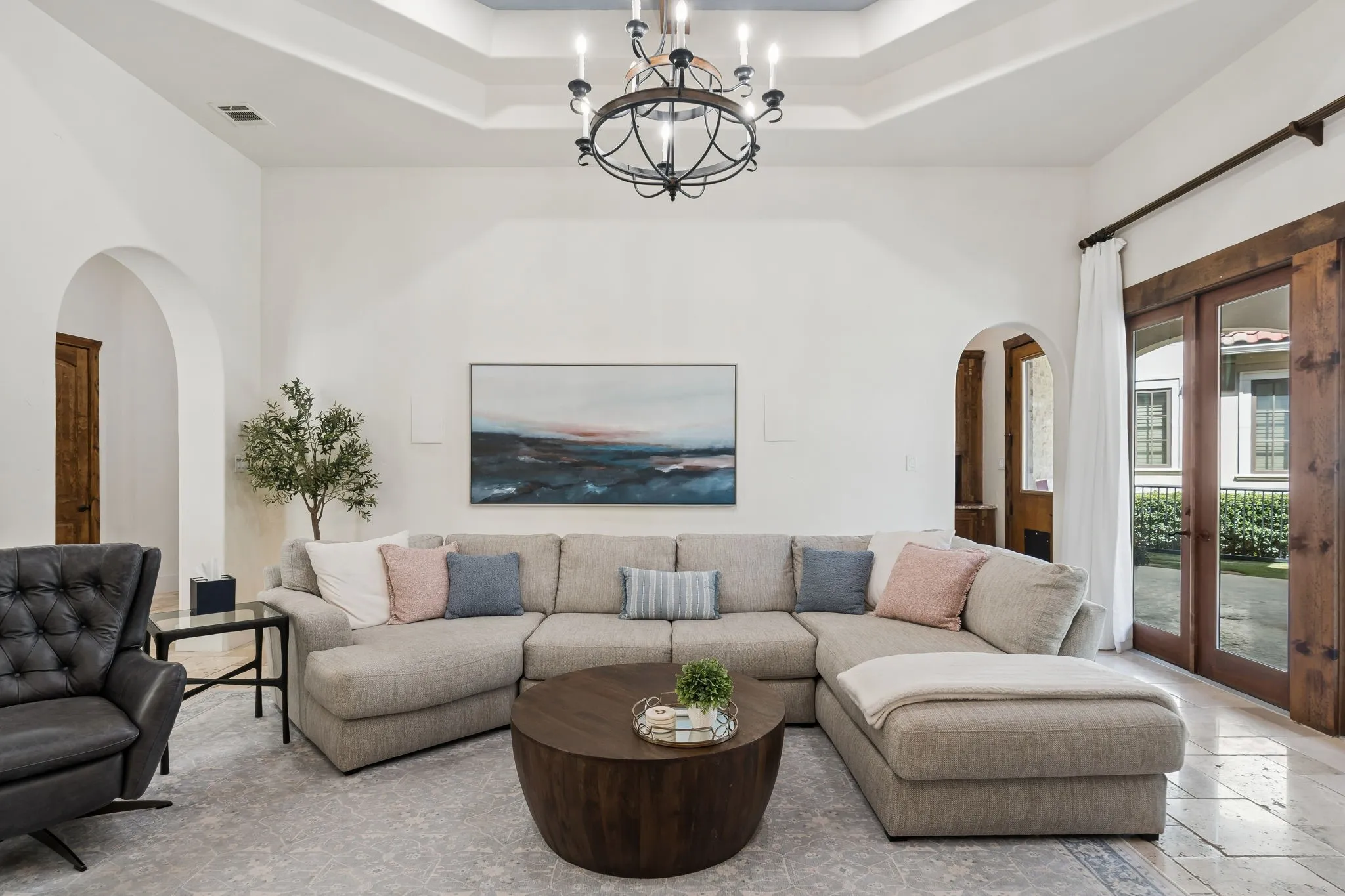 Tray ceiling with a decorative chandelier, arched doorways, and light-toned flooring