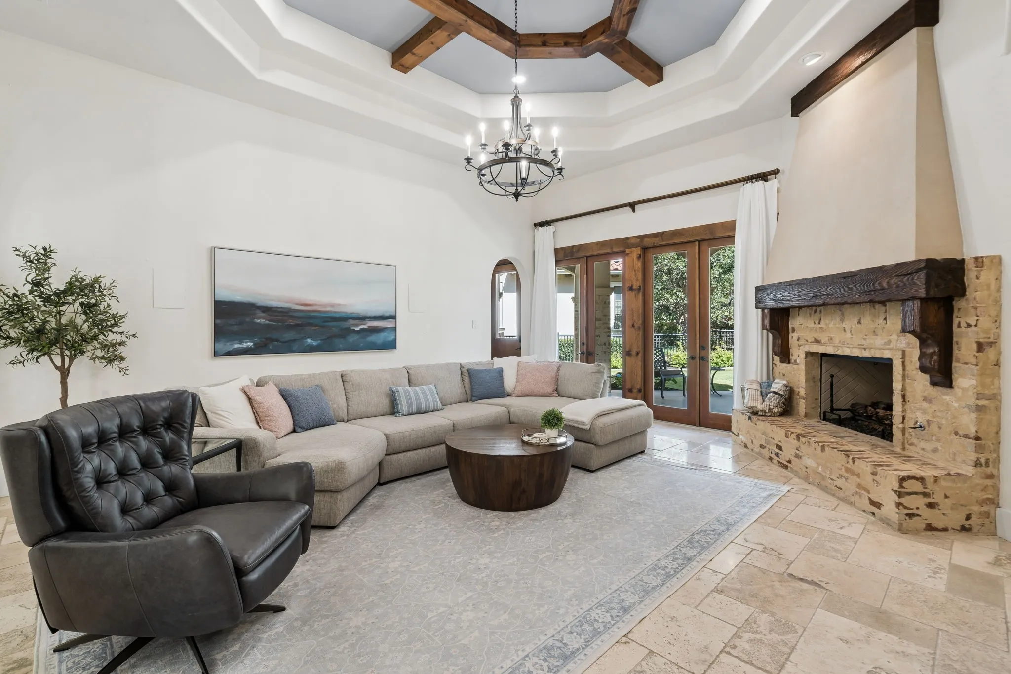 Vaulted ceiling with exposed wood beams, wrought iron chandelier, stone fireplace with a substantial wood mantel, tiled flooring, and wood-framed glass doors