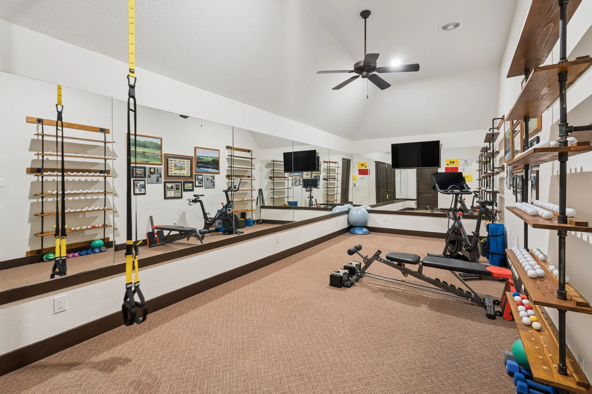 Full size gym or golf simulator room with high ceilings with a ceiling fan, full-wall mirrors, industrial-style shelving, and carpeted flooring