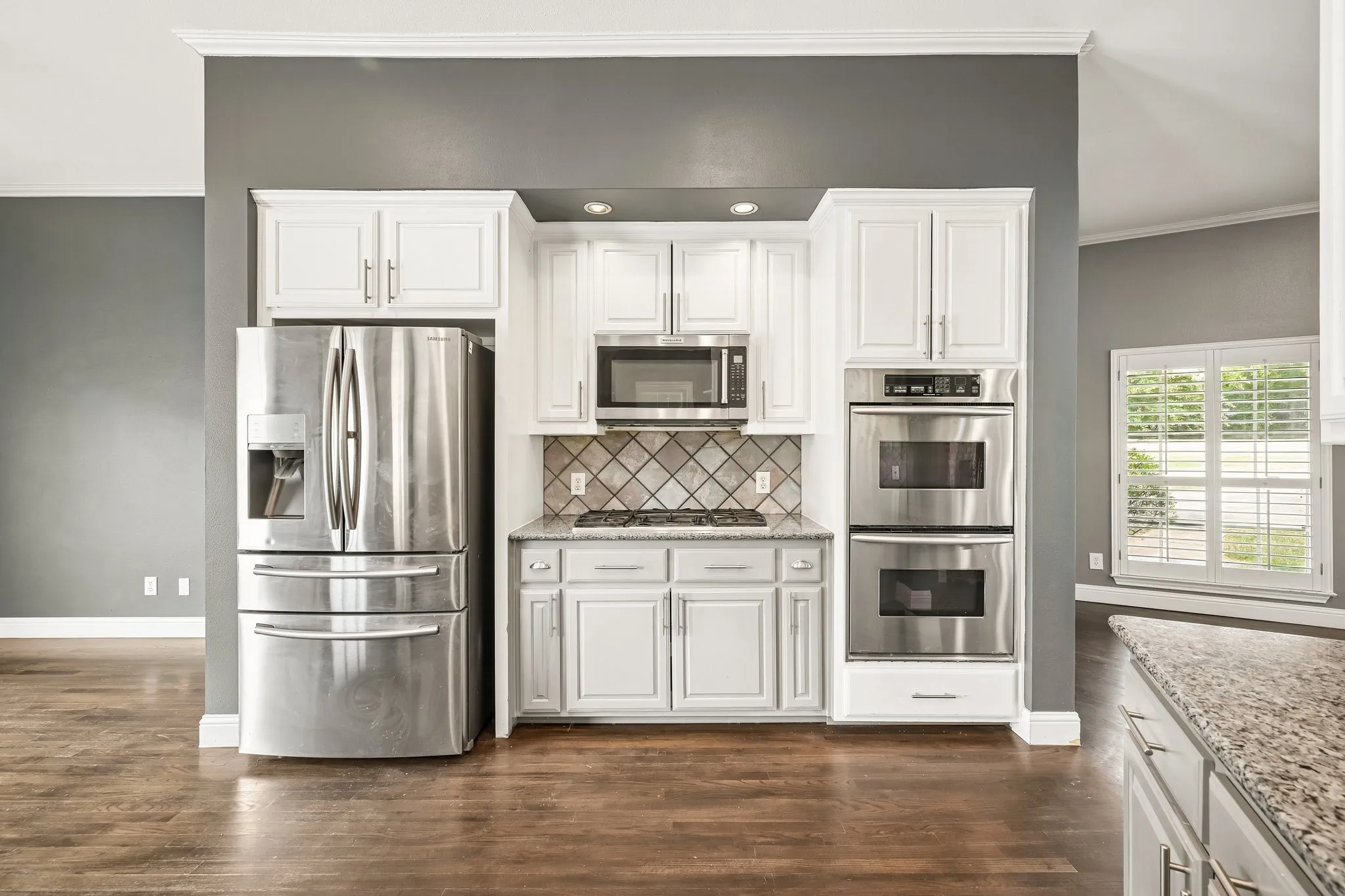 Chef's kitchen featuring white cabinetry, stainless steel French-door refrigerator, dual wall-mounted ovens, and a decorative tile backsplash