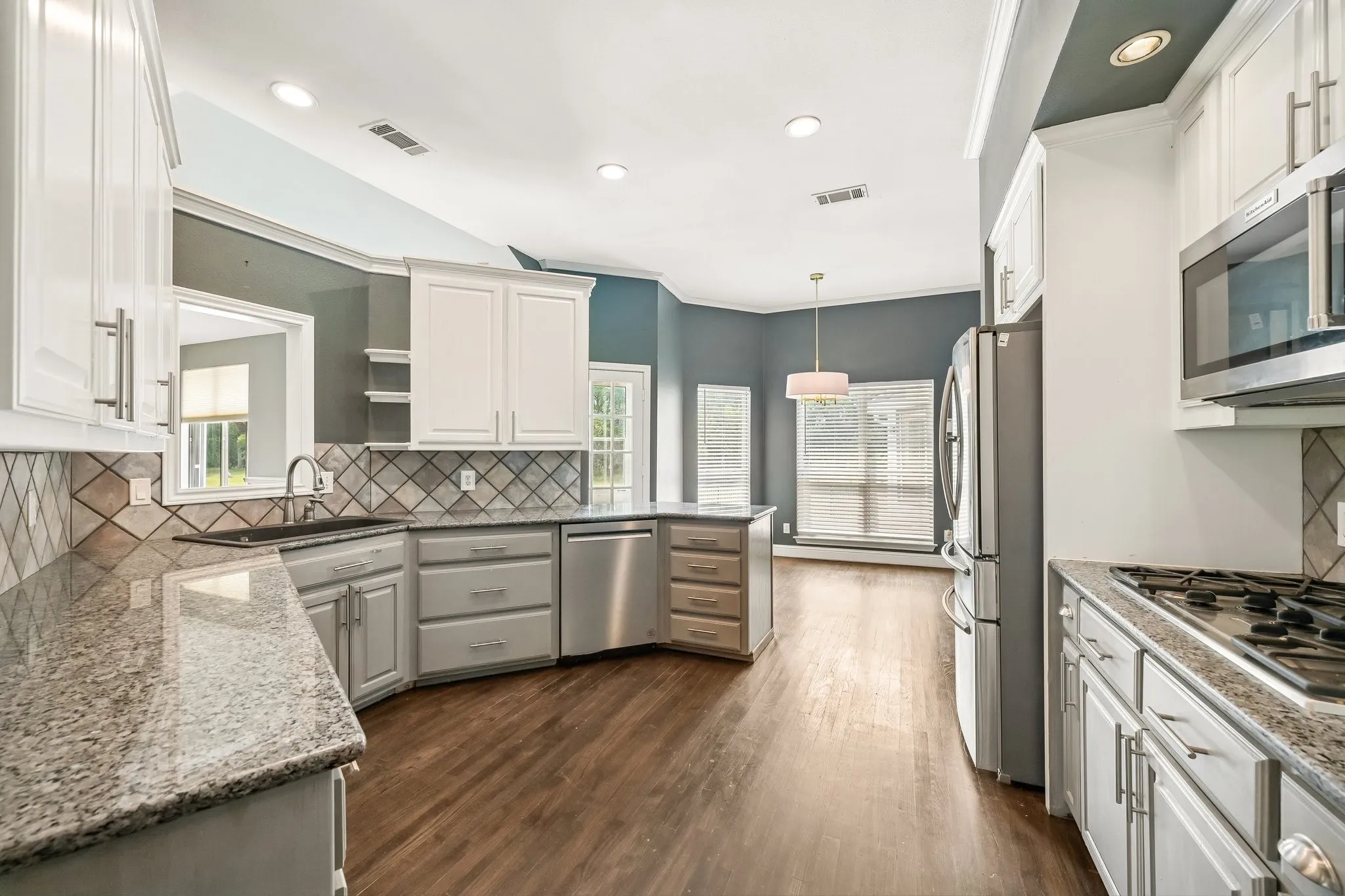 Kitchen featuring white cabinetry, granite countertops, stainless steel appliances, wood-finish flooring, and a decorative tile backsplash