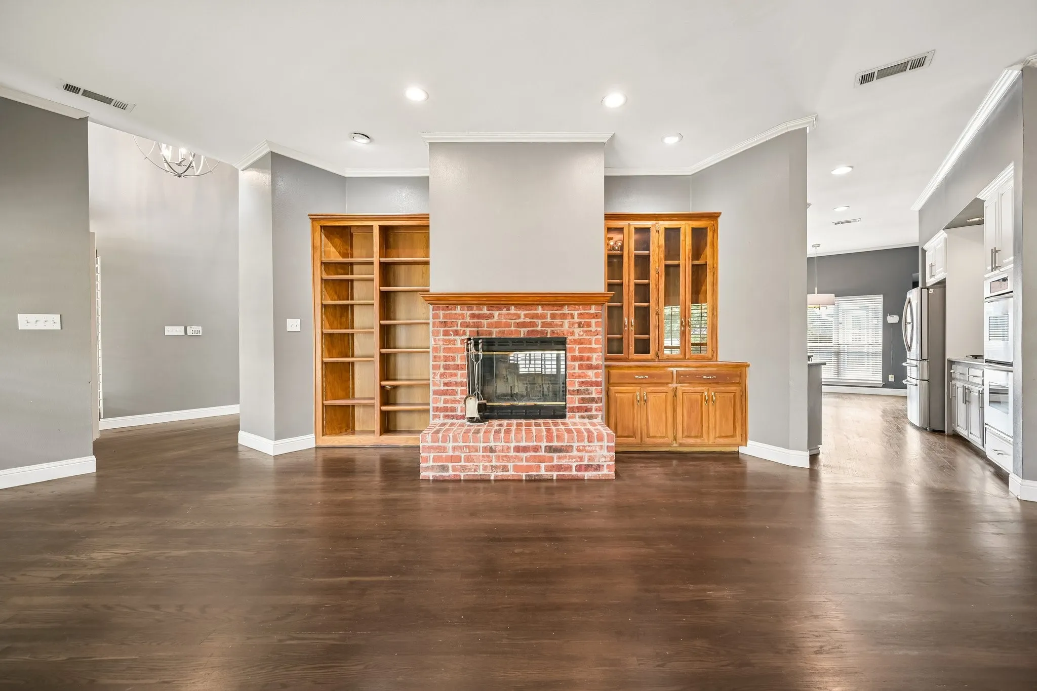 Spacious open-concept living area featuring dark wood-finish flooring, soaring ceilings with recessed lighting, and a striking brick fireplace with integrated hearth