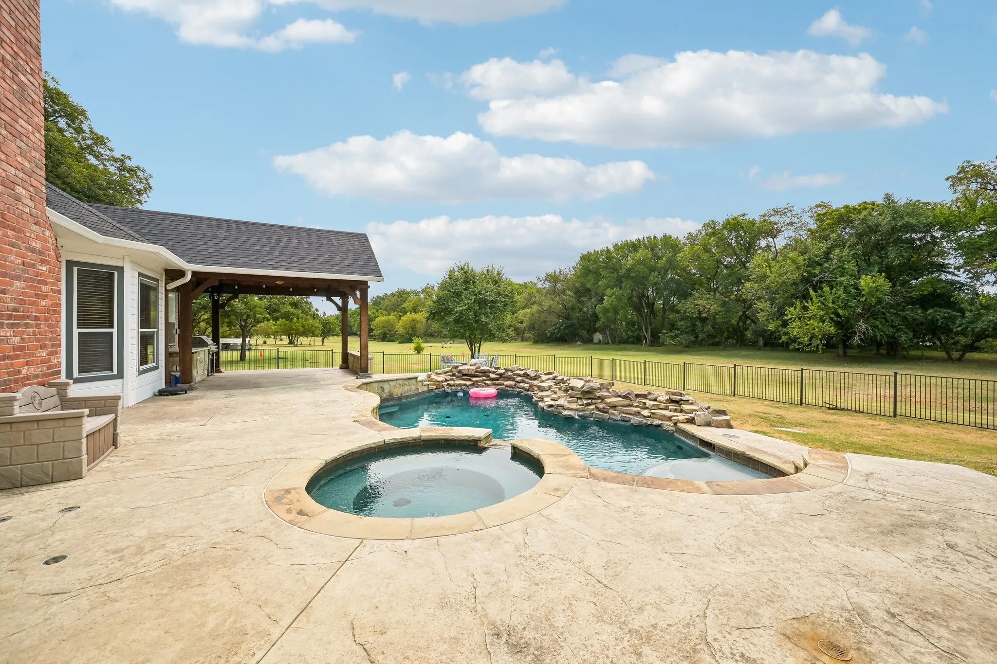 Stamped concrete patio with an integrated spa and freeform pool featuring a rock waterfall