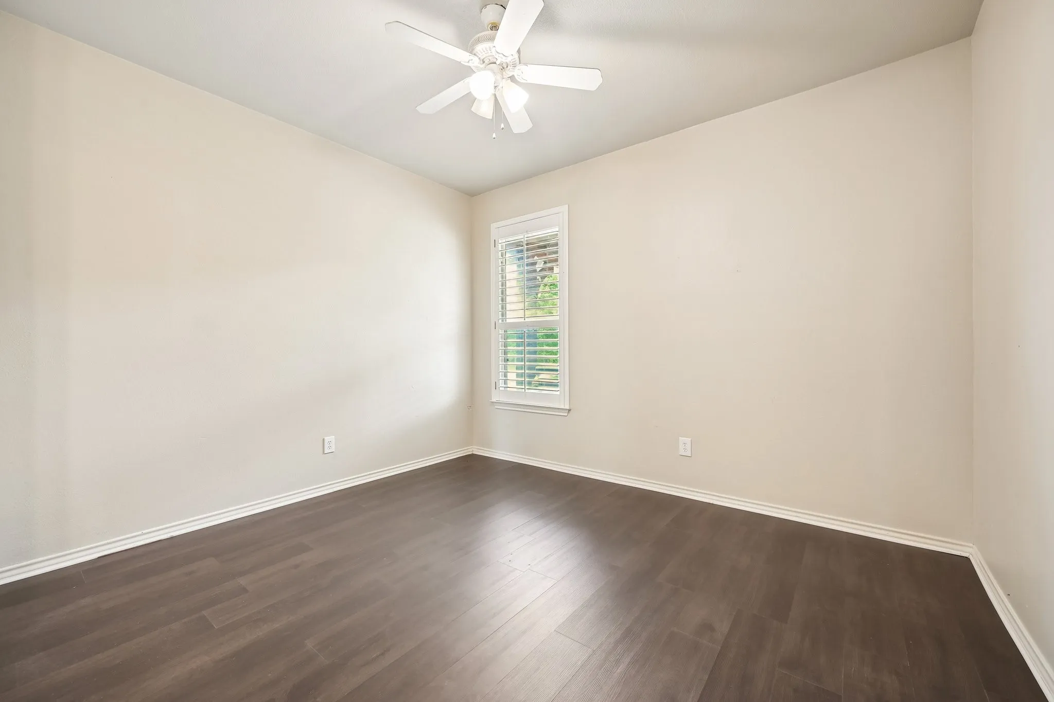 Bright and spacious bedroom featuring dark wood-finish flooring, neutral painted walls, and a ceiling fan with integrated lighting
