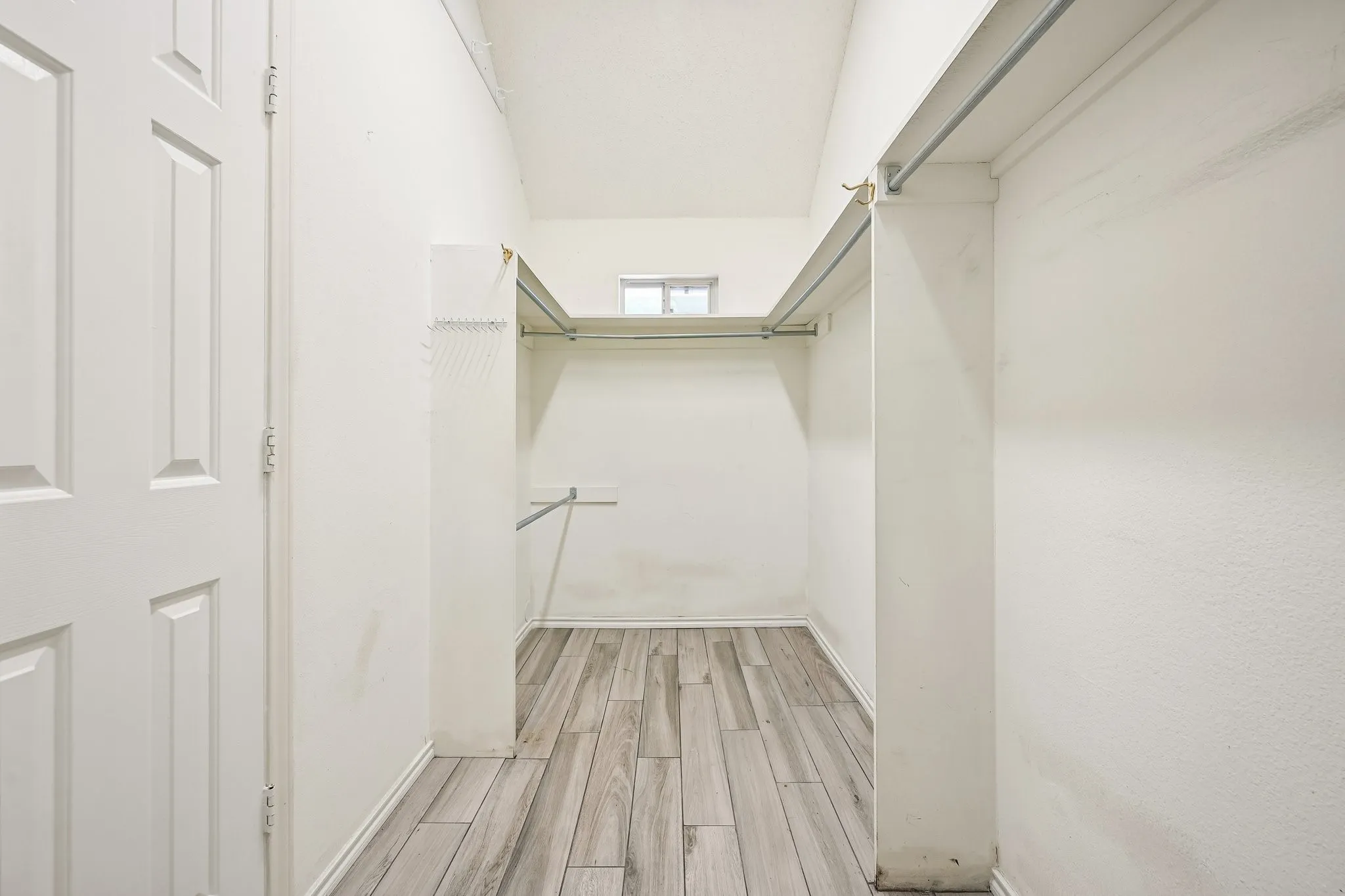 Walk-in closet featuring wood-finish flooring, multiple hanging rods, and a high window