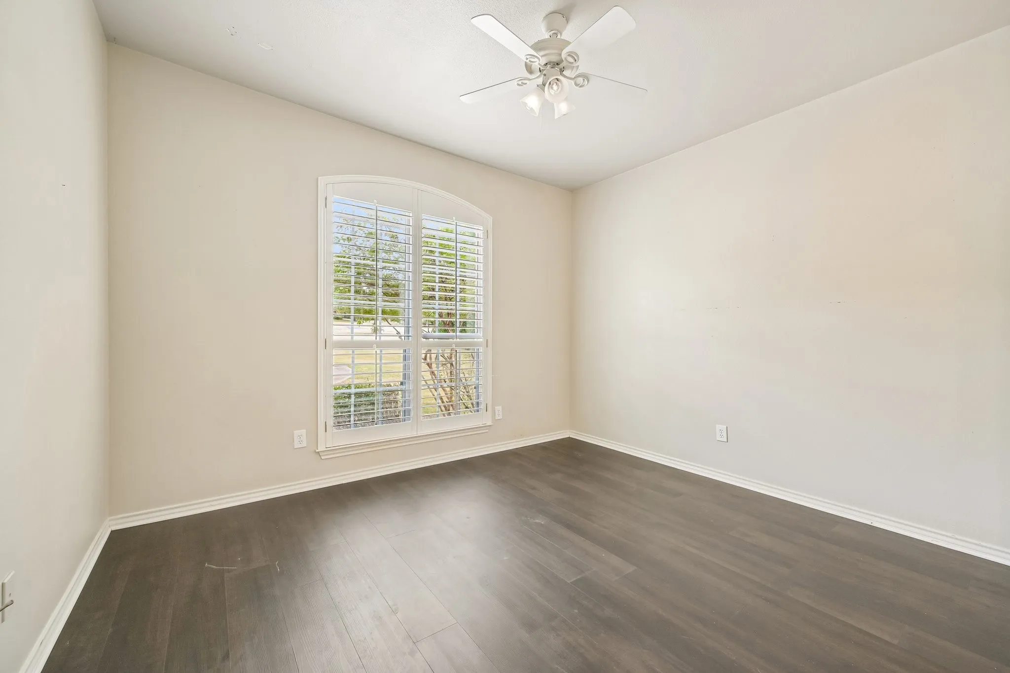 Arched window with plantation shutters, wood-finish flooring, and a ceiling fan with integrated lighting