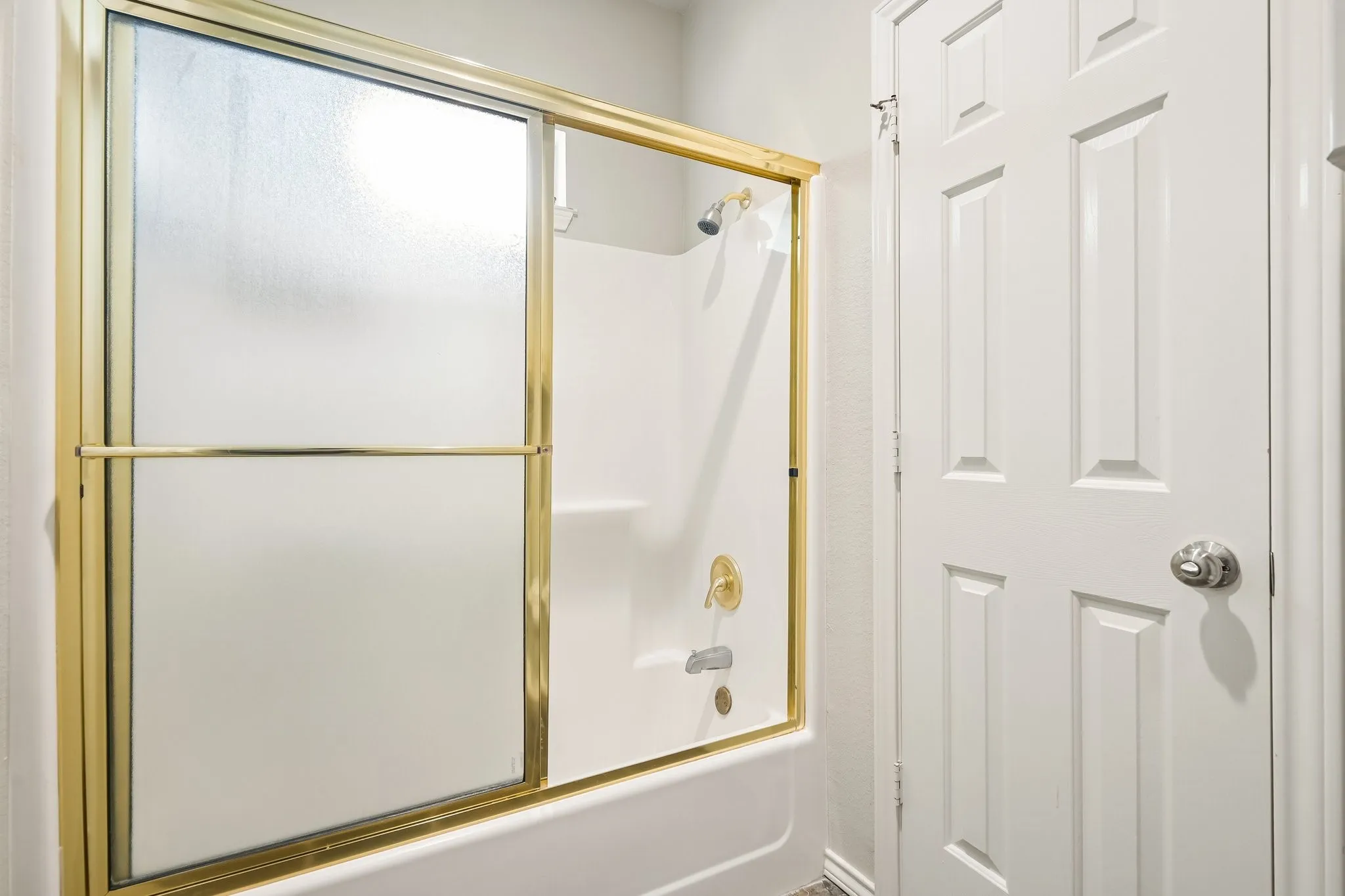 Bathtub with an integrated shower, gold-toned shower door frame, and white paneled door