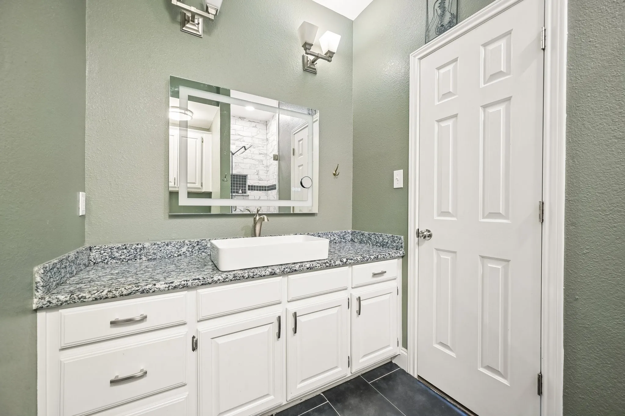 White vanity with ample cabinetry, granite countertop, rectangular vessel sink, and an illuminated mirror