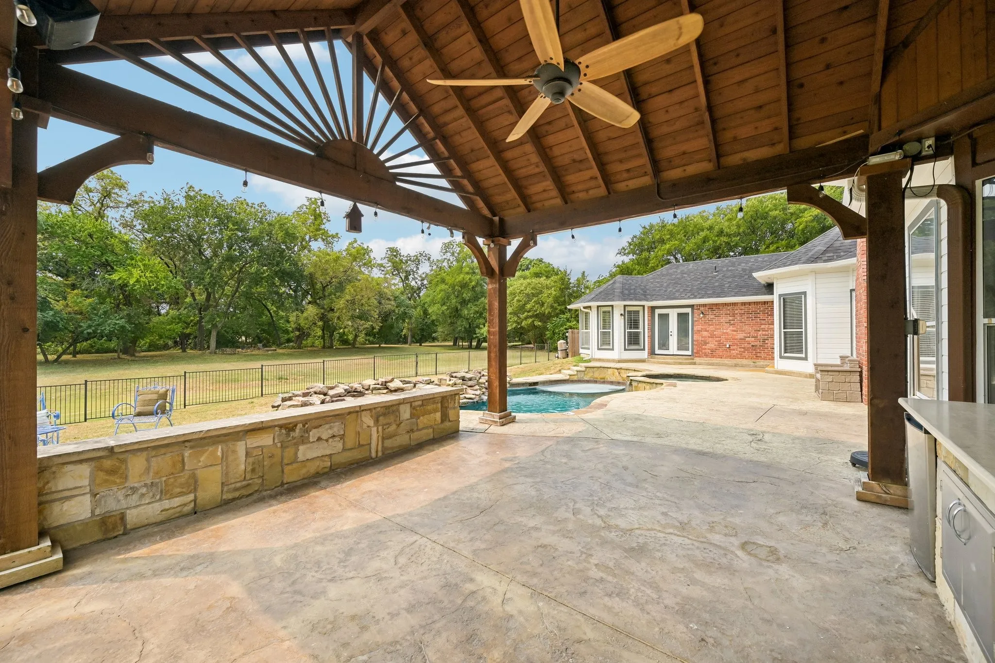 Expansive covered patio with a wood-plank ceiling, ceiling fan, and string lighting