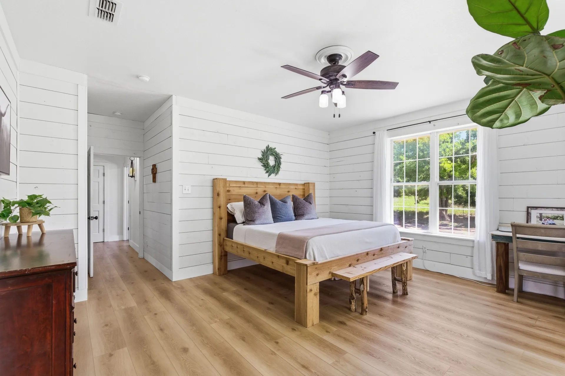 Wood-finish flooring, white shiplap walls, ceiling fan with integrated lighting, and a large multi-pane window