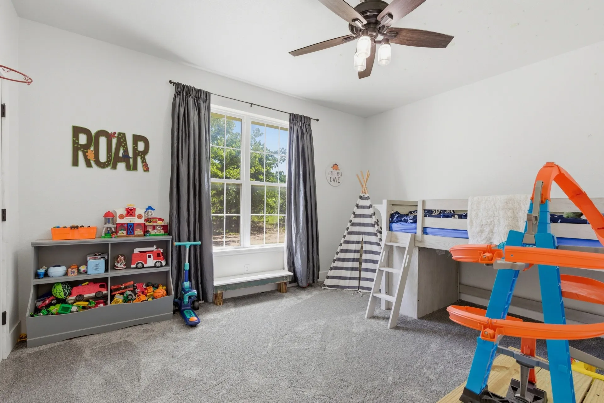 Light gray carpet flooring, white painted walls, a large window with white framing, and a ceiling fan with integrated lighting