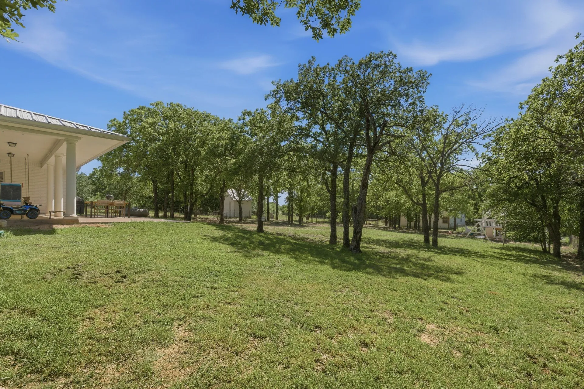 Expansive outdoor area with a covered patio, multiple mature trees, and a manicured lawn
