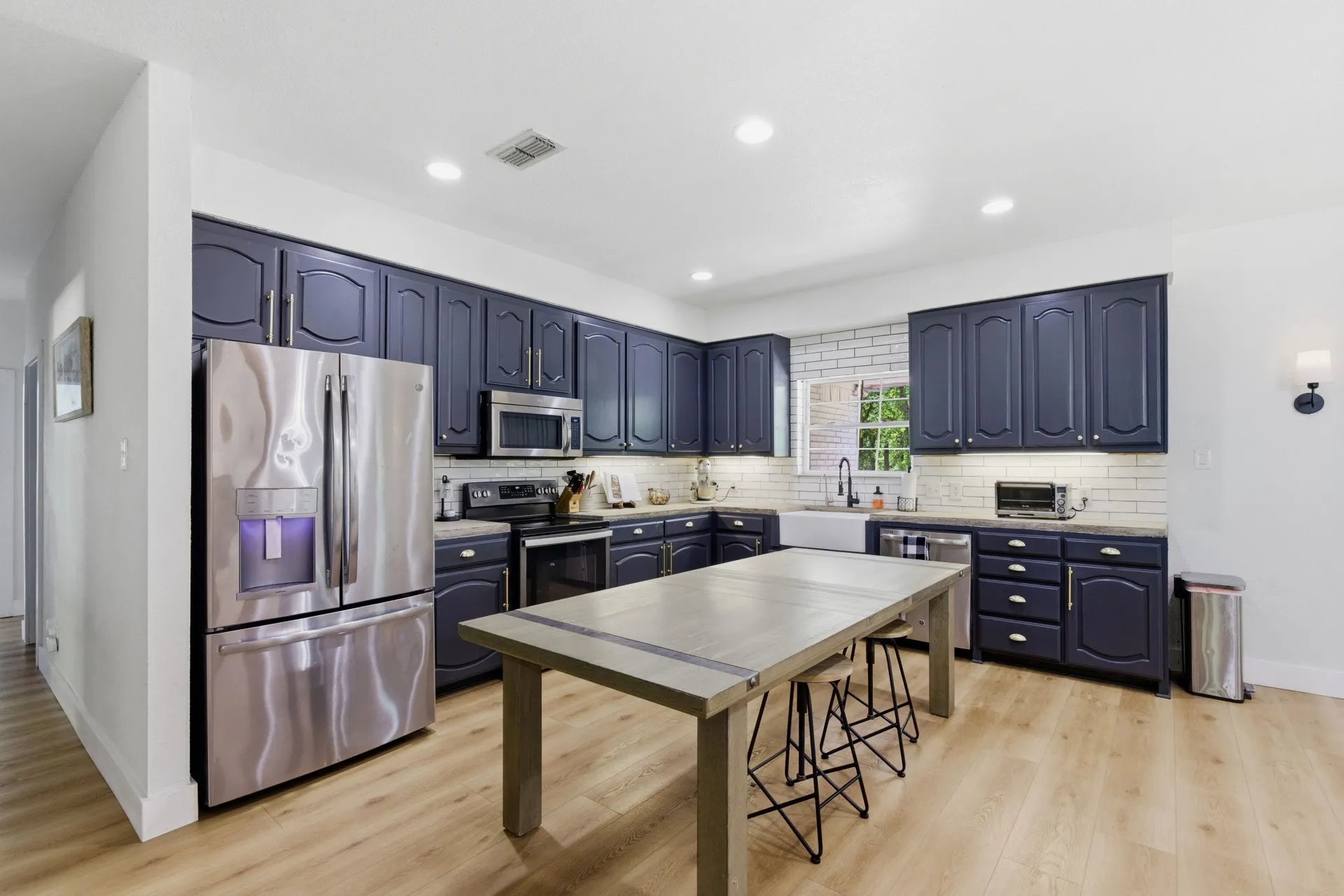 Kitchen featuring dark cabinetry, stainless steel appliances, a white brick-patterned backsplash, and wood-finish flooring