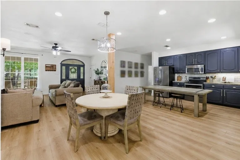 Wood-finish flooring throughout, kitchen featuring dark cabinetry with stainless steel appliances, a large island with seating, recessed lighting, and a decorative chandelier