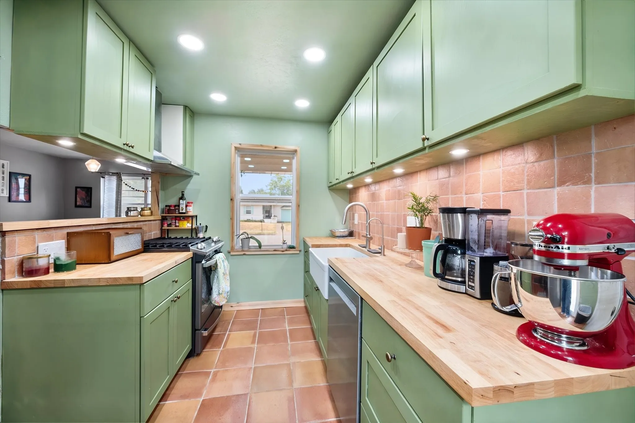 Galley kitchen featuring sage green cabinetry, butcher block countertops, terracotta tile flooring, a farmhouse sink, and recessed lighting