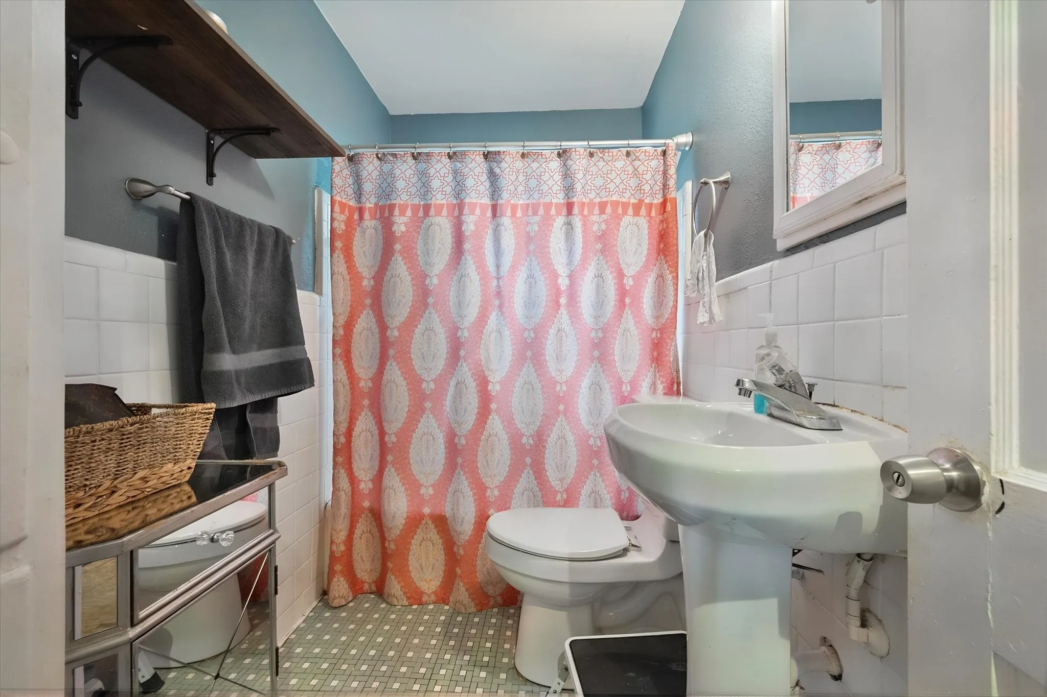 Pedestal sink with chrome faucet, white tiled walls, and mosaic-style flooring