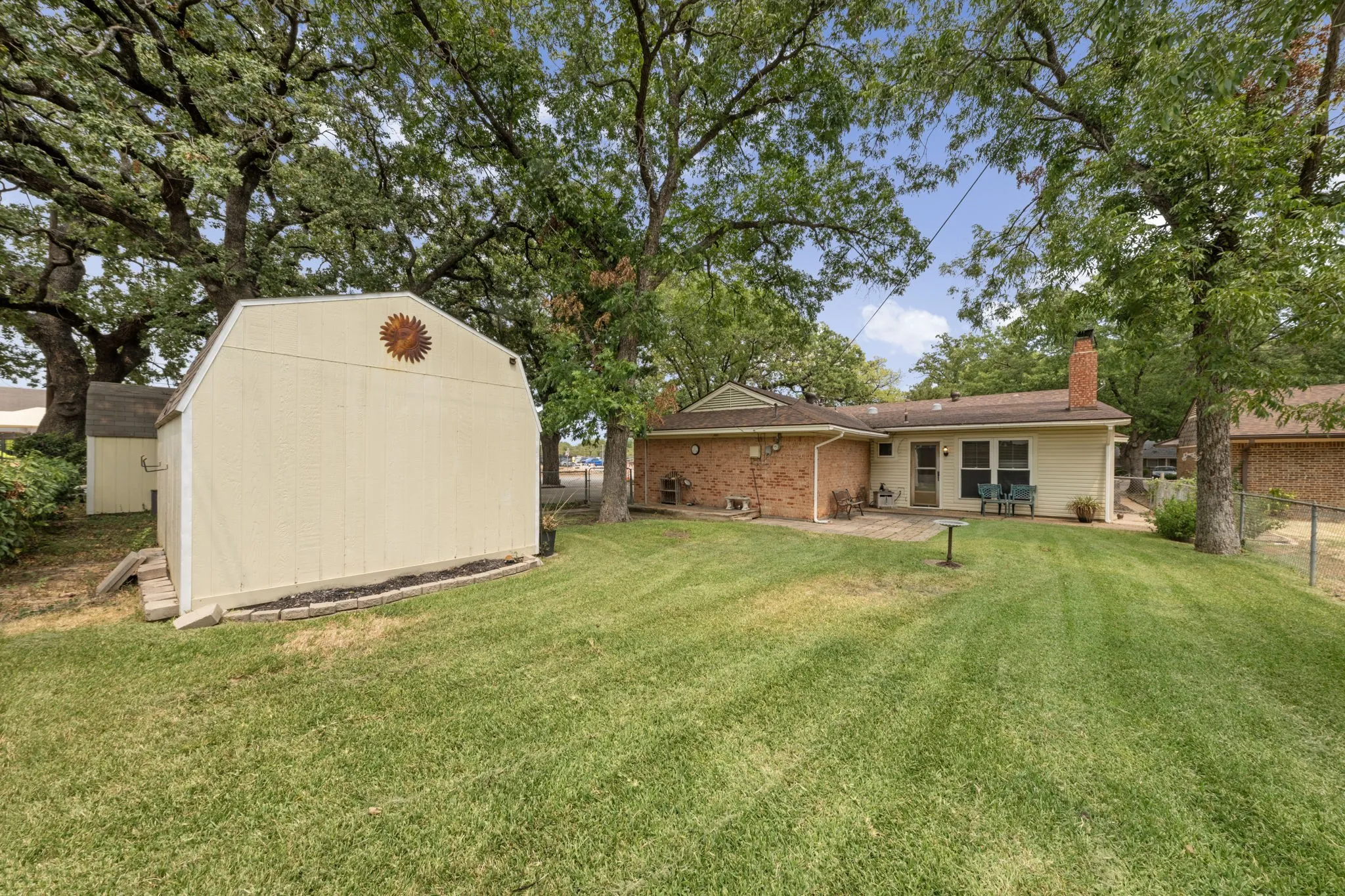 Expansive rear yard featuring mature trees, a detached storage shed, a brick exterior with siding, a brick chimney, and a concrete patio