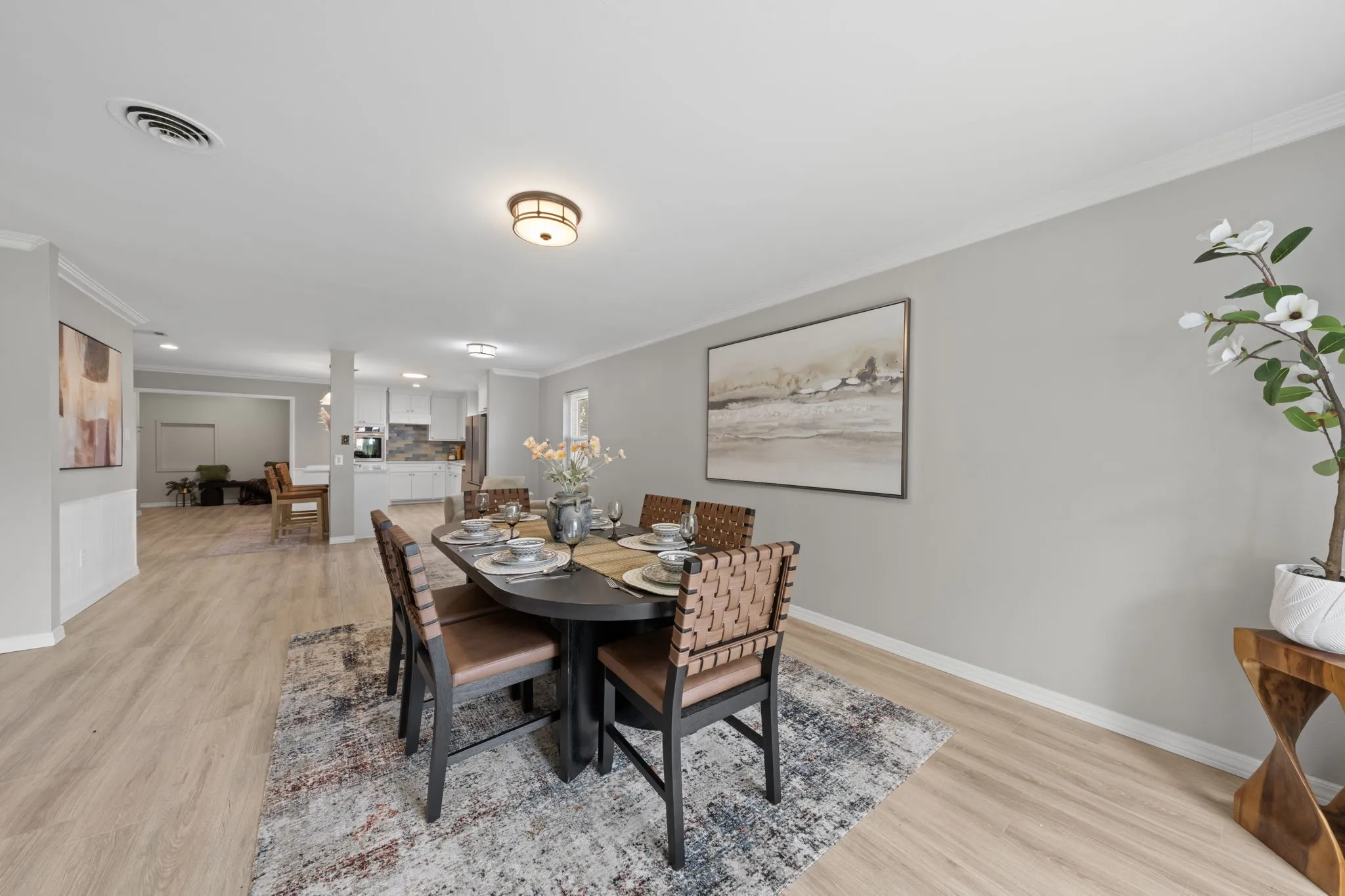 Open-concept living area featuring light-toned wood-finish flooring, a contemporary ceiling light fixture, and crown molding