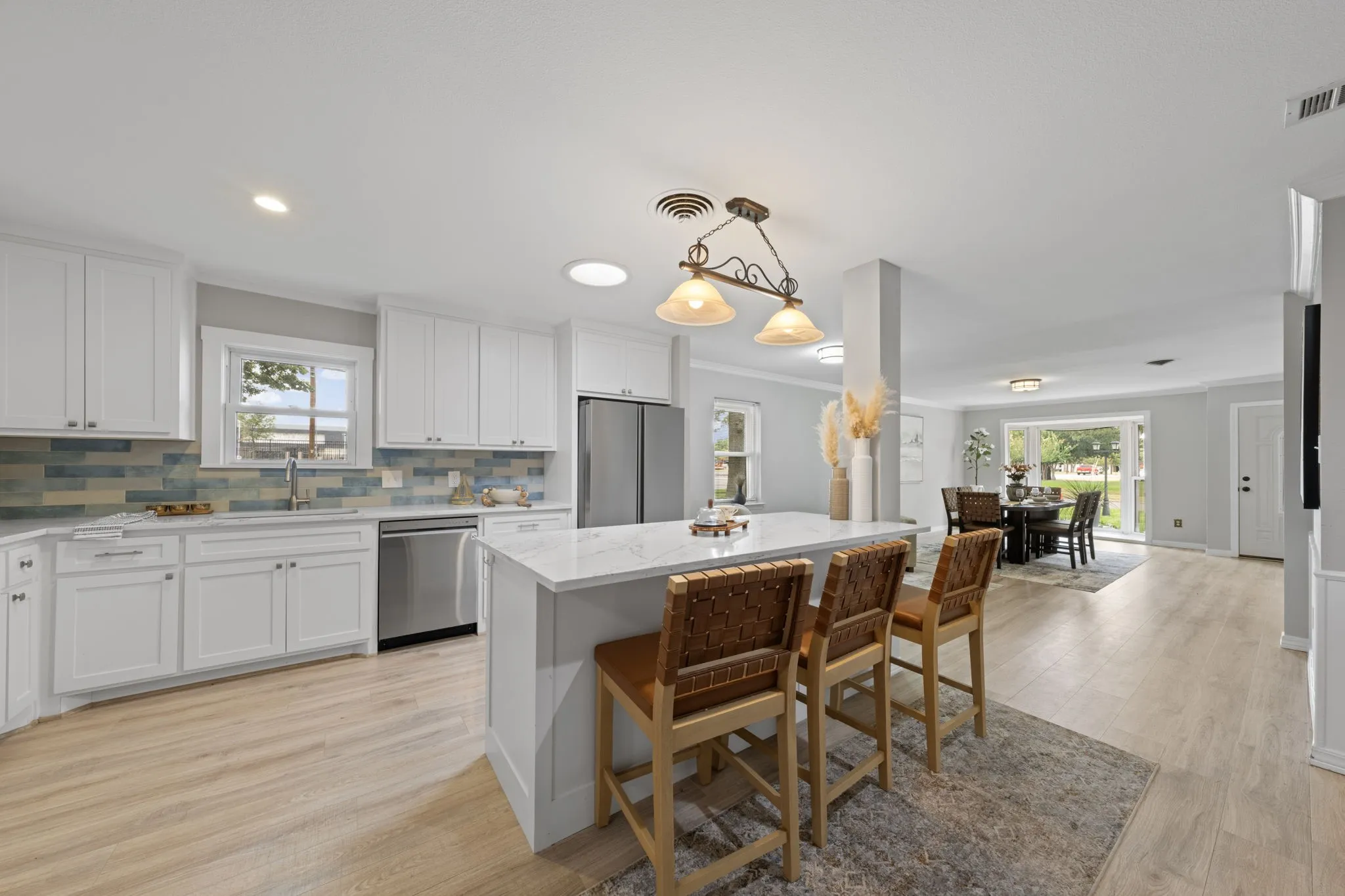 Kitchen featuring white shaker cabinetry, stainless steel appliances, a white stone-finish island with seating, and a decorative tile backsplash