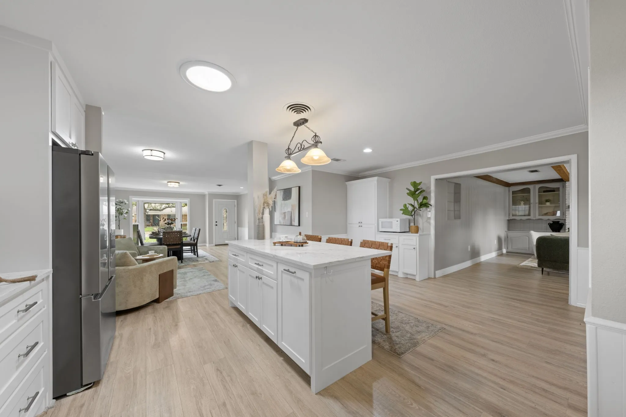 Kitchen featuring wood-finish flooring, white cabinetry, a kitchen island with seating, a skylight, and a stainless steel refrigerator