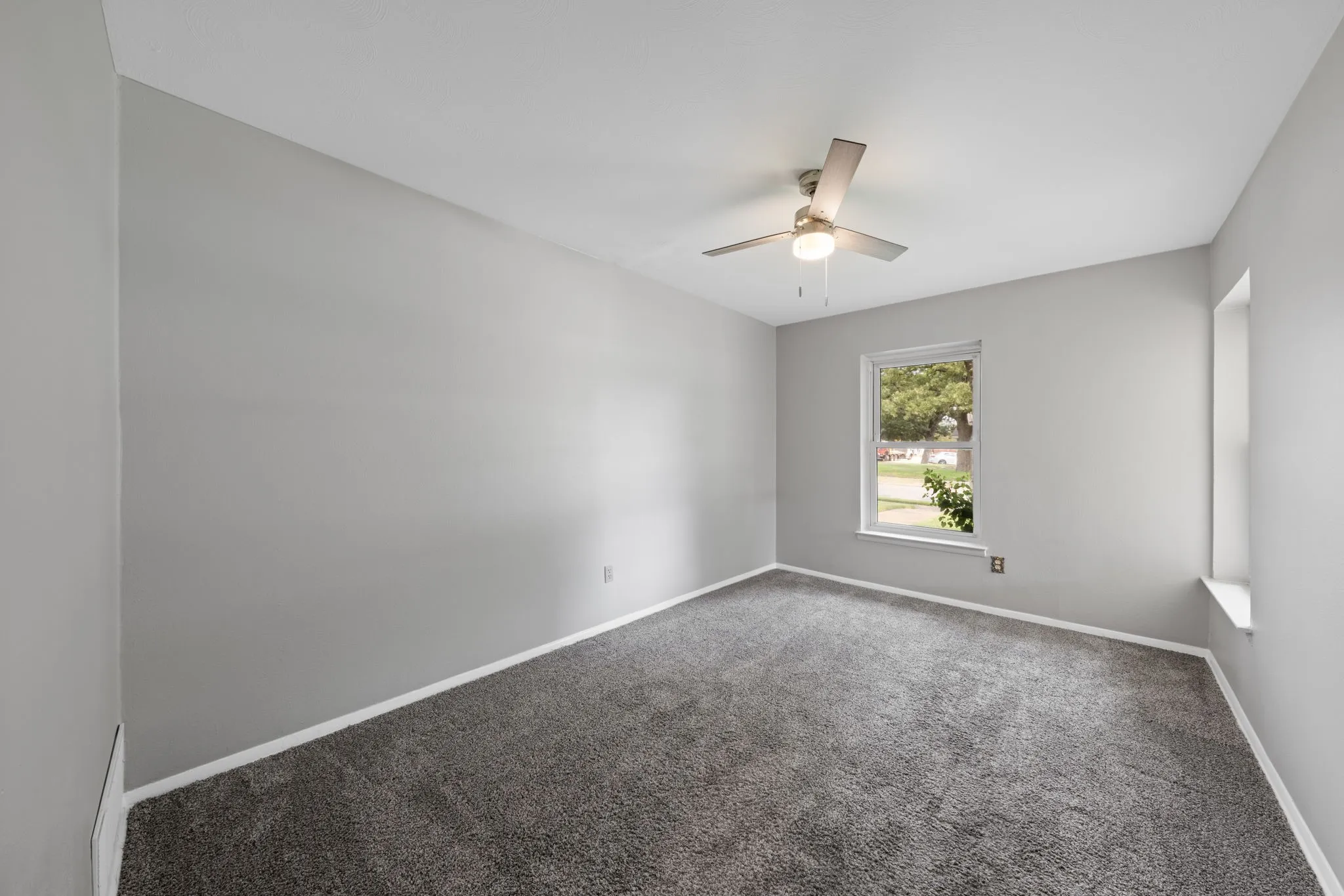 Plush gray carpeting with light gray walls, featuring a ceiling fan with integrated lighting